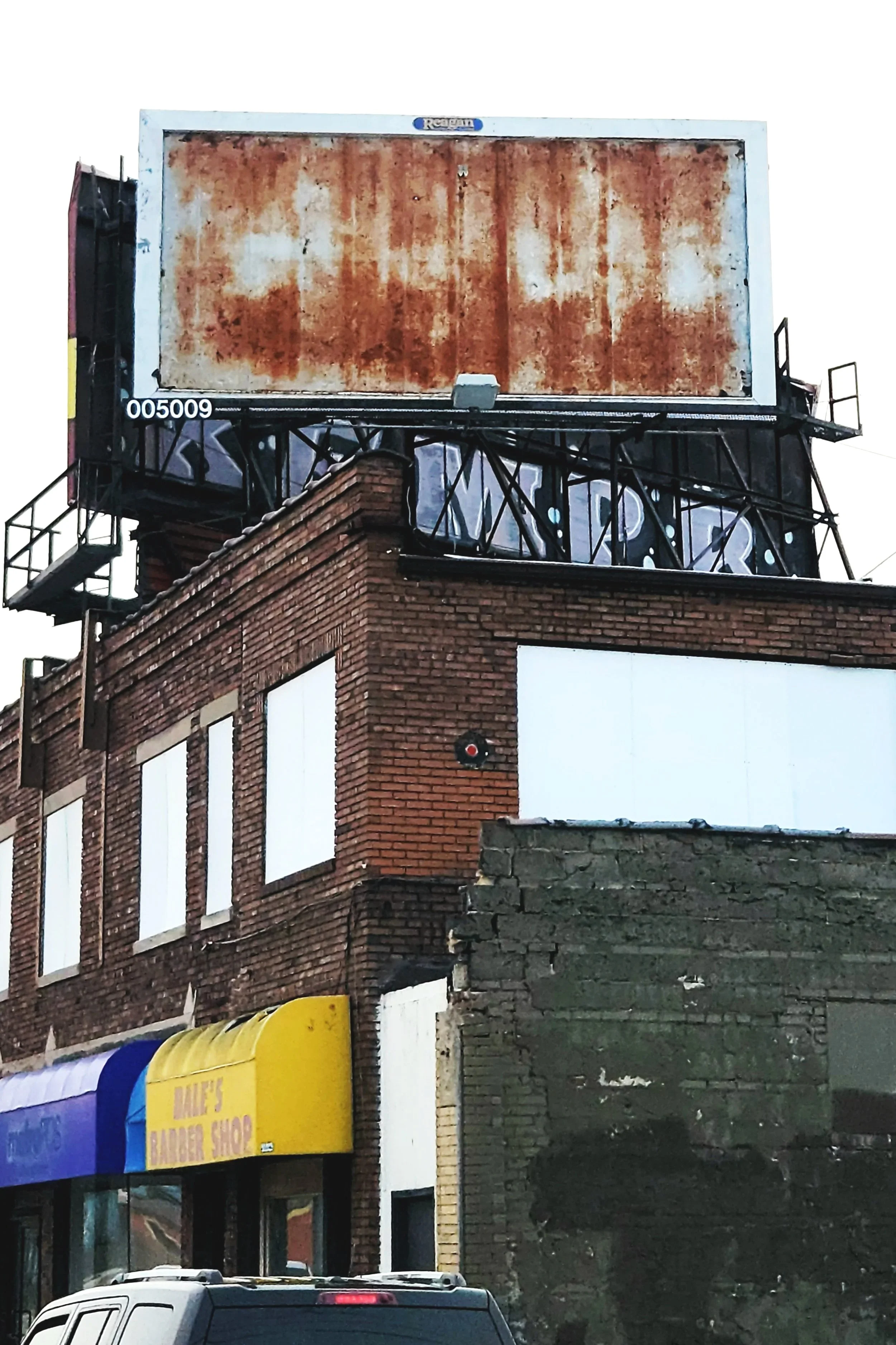 Weathered rusted billboard above an old brick building photographed from a stoplight against a bright sky.