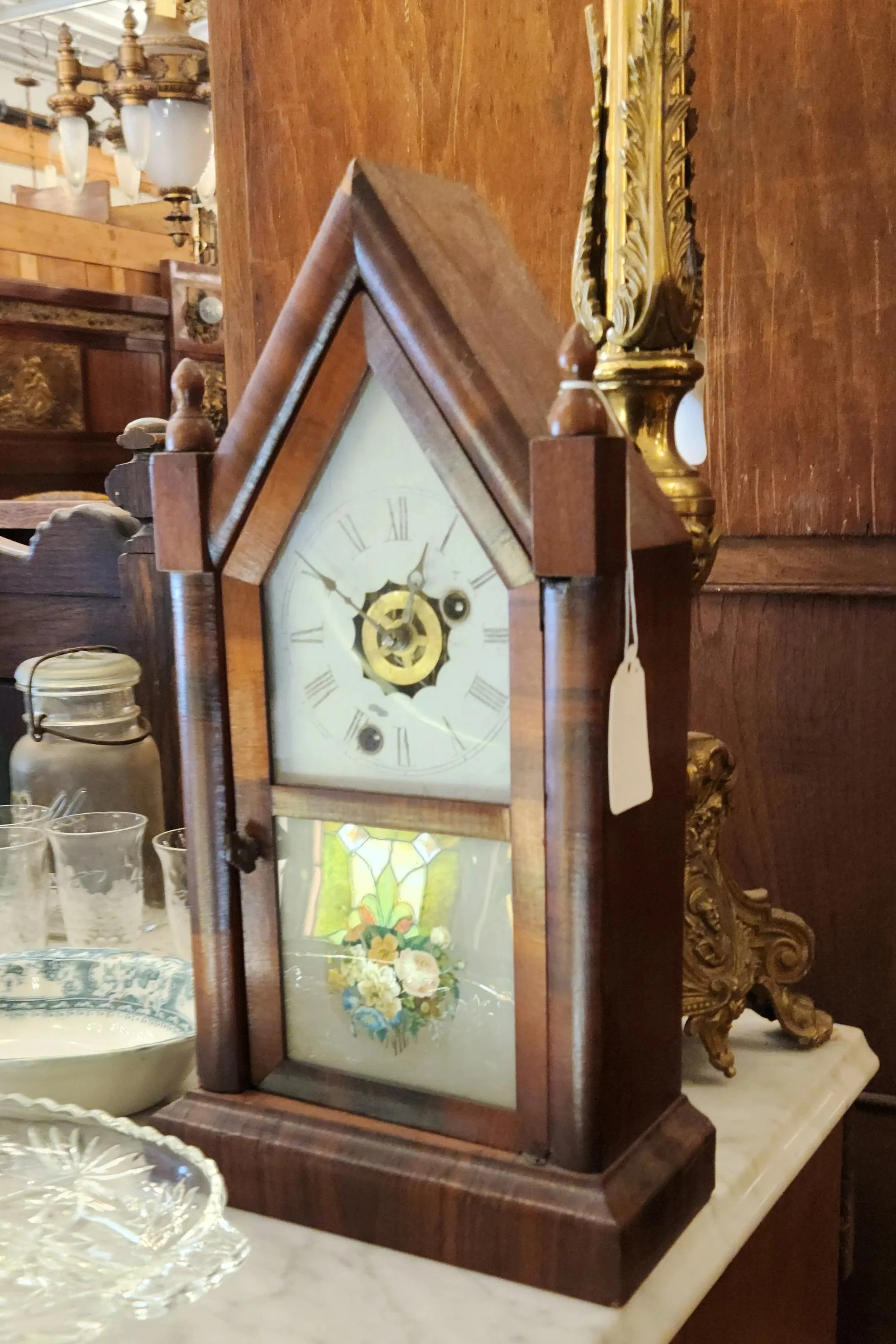 Antique wooden mantel clock with glass front displayed among vintage objects in an antique shop.
