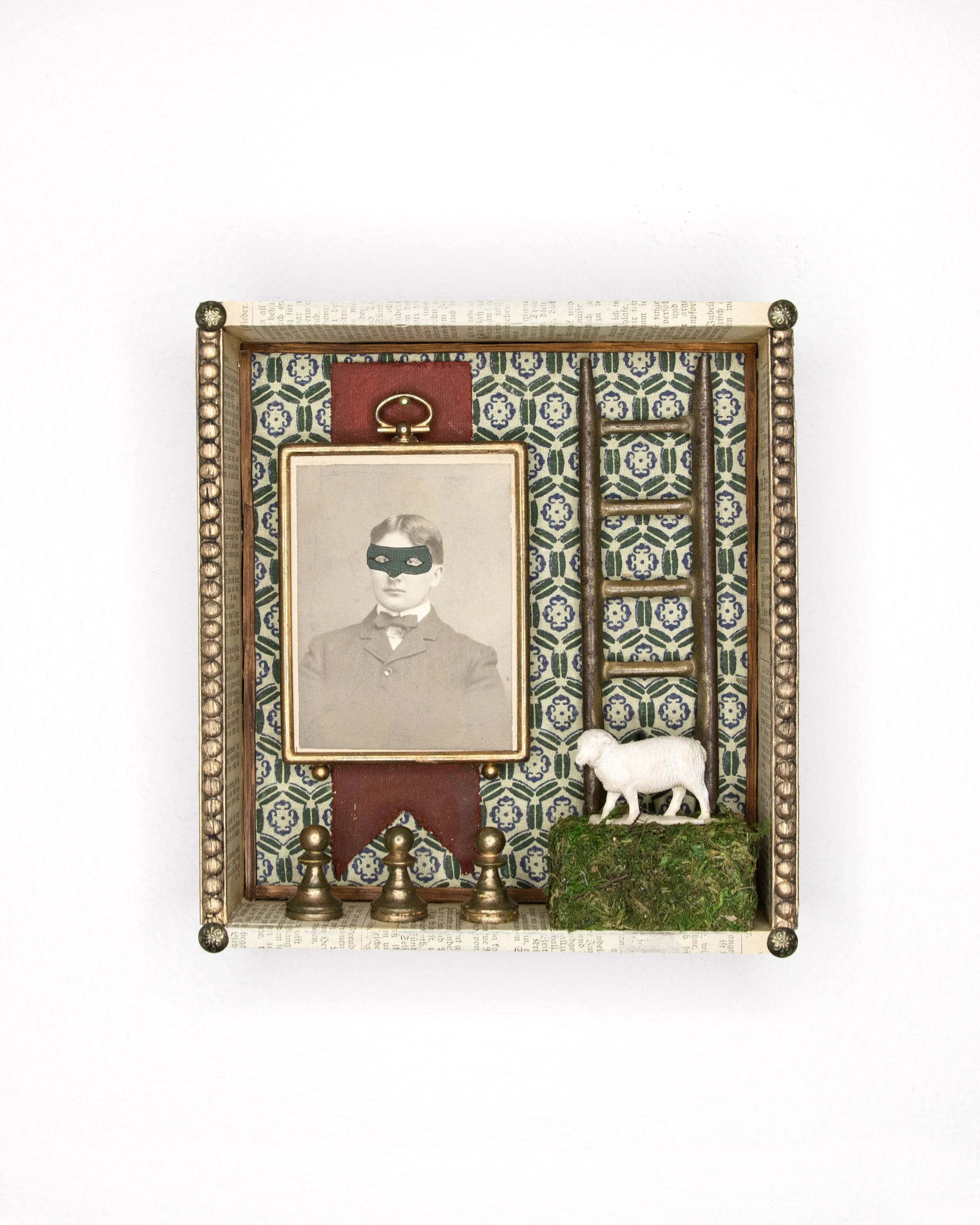 Wooden cigar box with an antique portrait of a man in a mask, a sheep on a grassy cube, a red ribbon and 3 golden chess pawns with a green patterned background