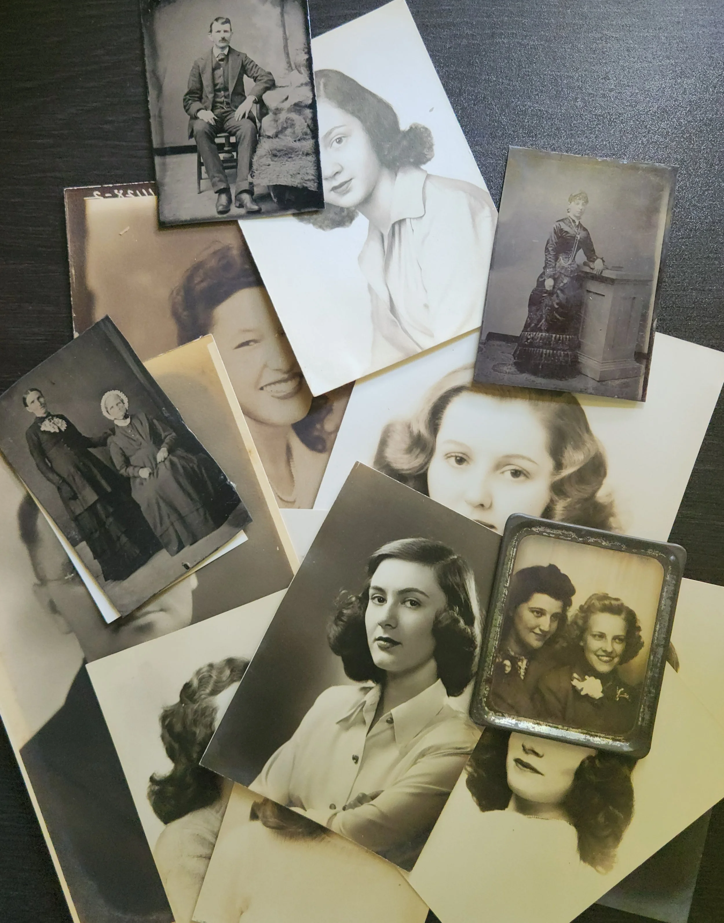 A collection of vintage black-and-white photographs scattered across a weathered wooden table, showing portraits and family snapshots from decades past.