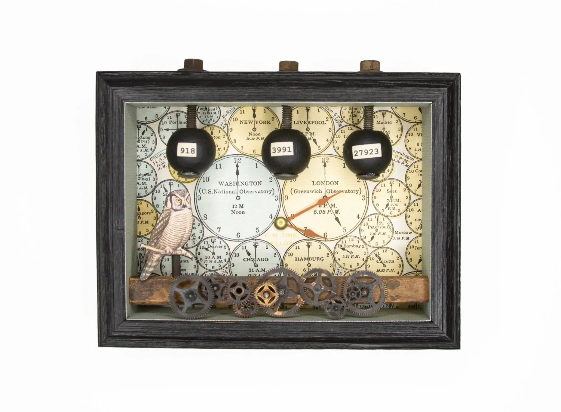 Assemblage artwork in a black shadow-box frame featuring a vintage world clock face background. Three hanging black weights labeled with numbers descend from the top, while an owl stands near the lower left. Rusted clock gears line the bottom edge, a