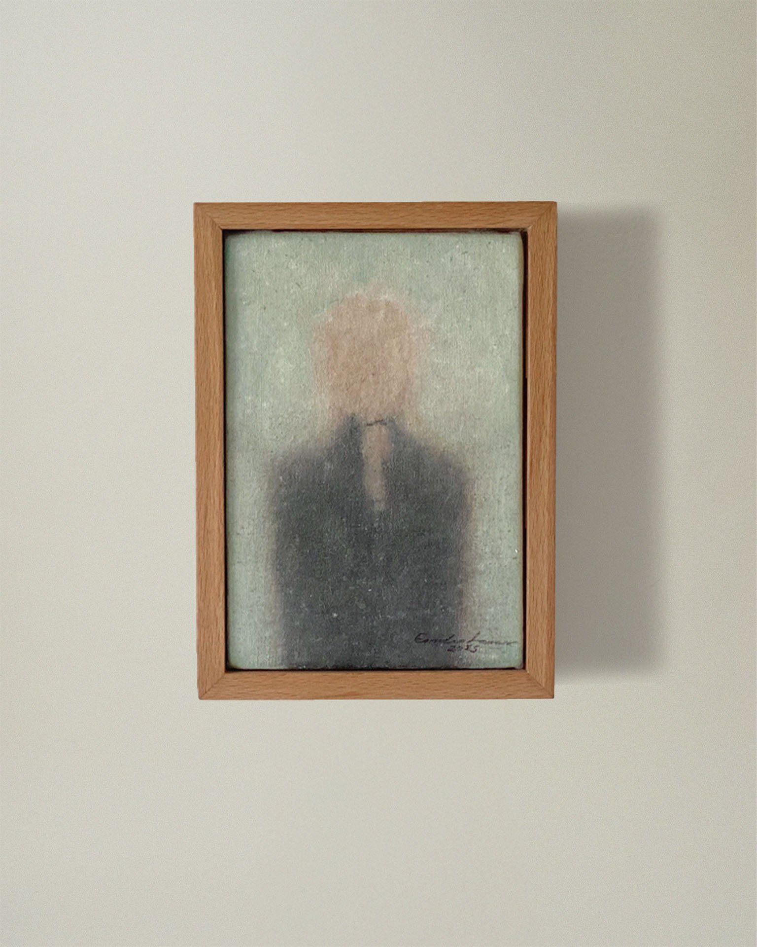 Tu – Sans titre by Emilia Lemaire, 2025. A blurred woman seen from behind, her blonde hair in a loose ponytail, in dark clothes against a pale grey-green ground, in a light oak frame.