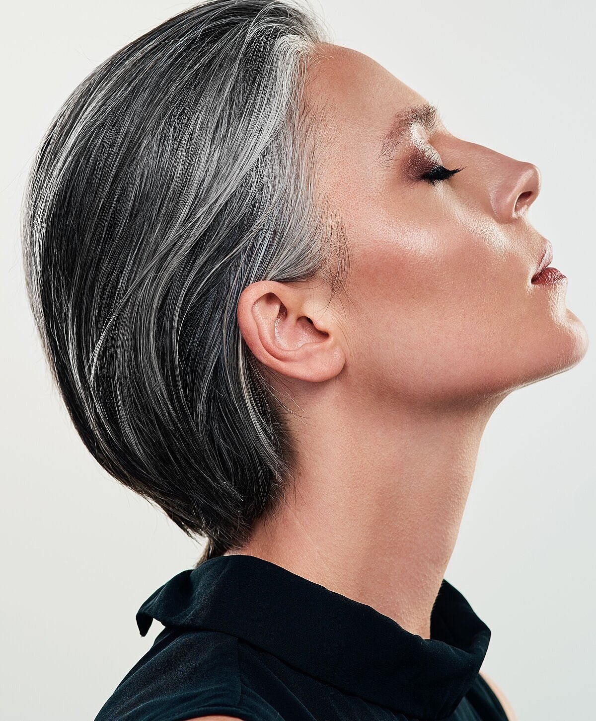 Side profile of a woman with gray hair and smooth skin, wearing a black top, with her eyes closed.