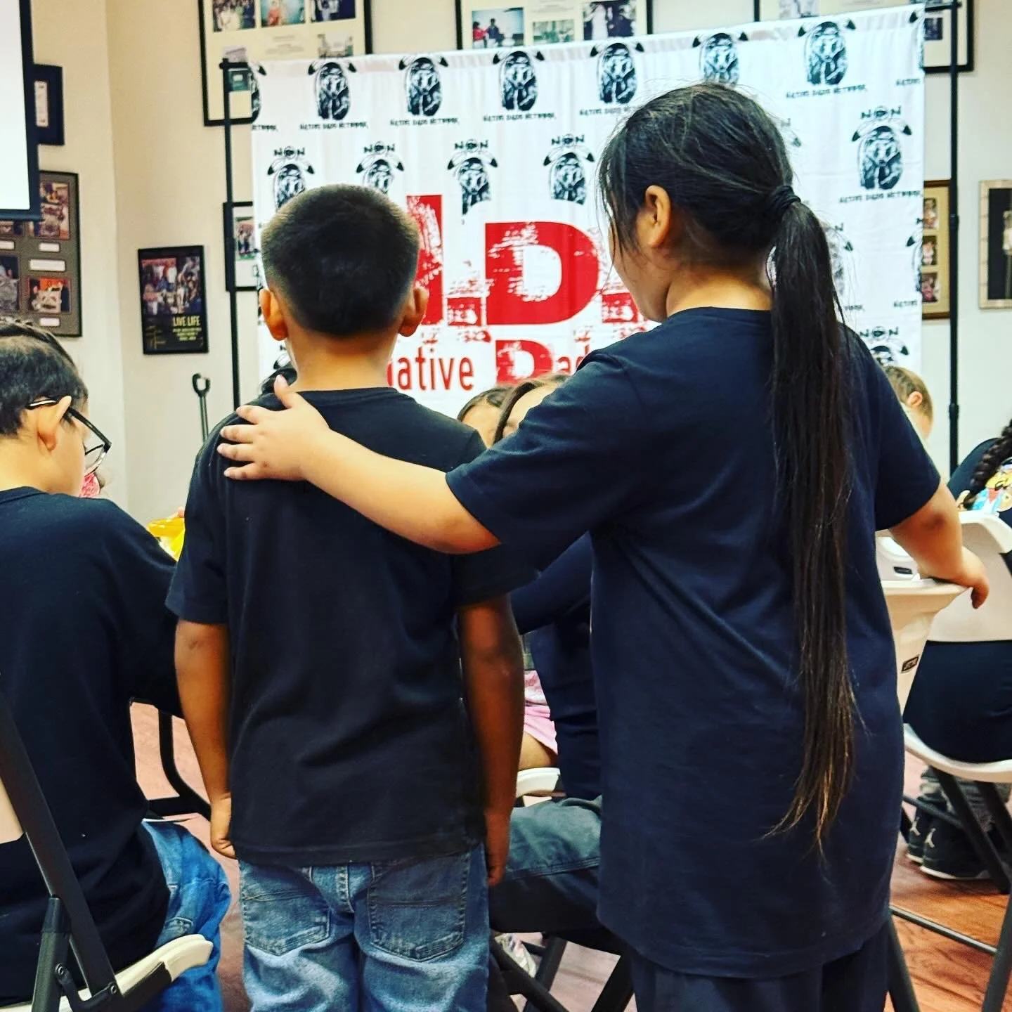 Children wearing black t-shirts in a room with a banner that reads 'Active Democracy' and covers a wall with pictures.