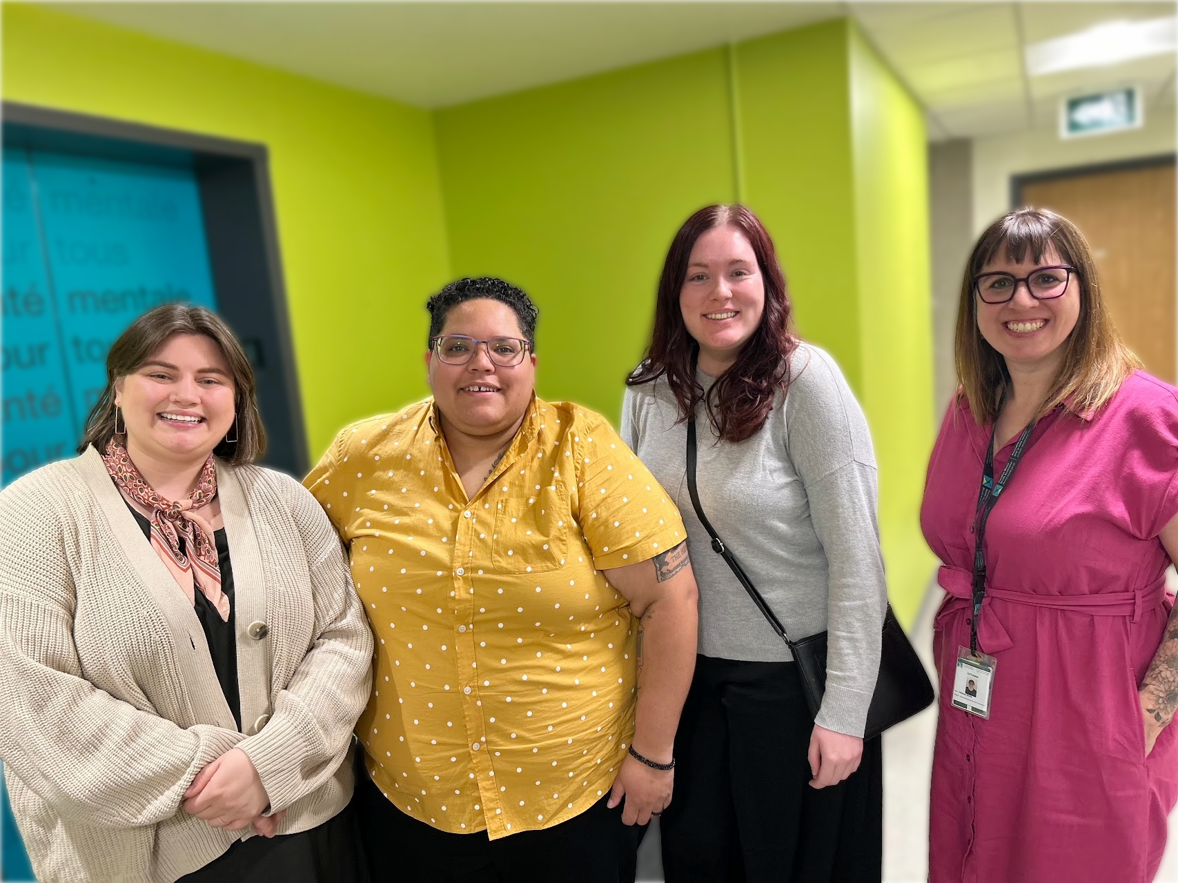 Four people smiling together against a green wall.