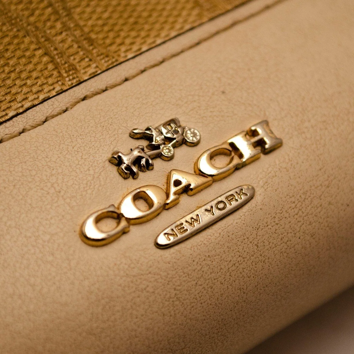 Close-up of a gold Coach logo with a horse and carriage, and a