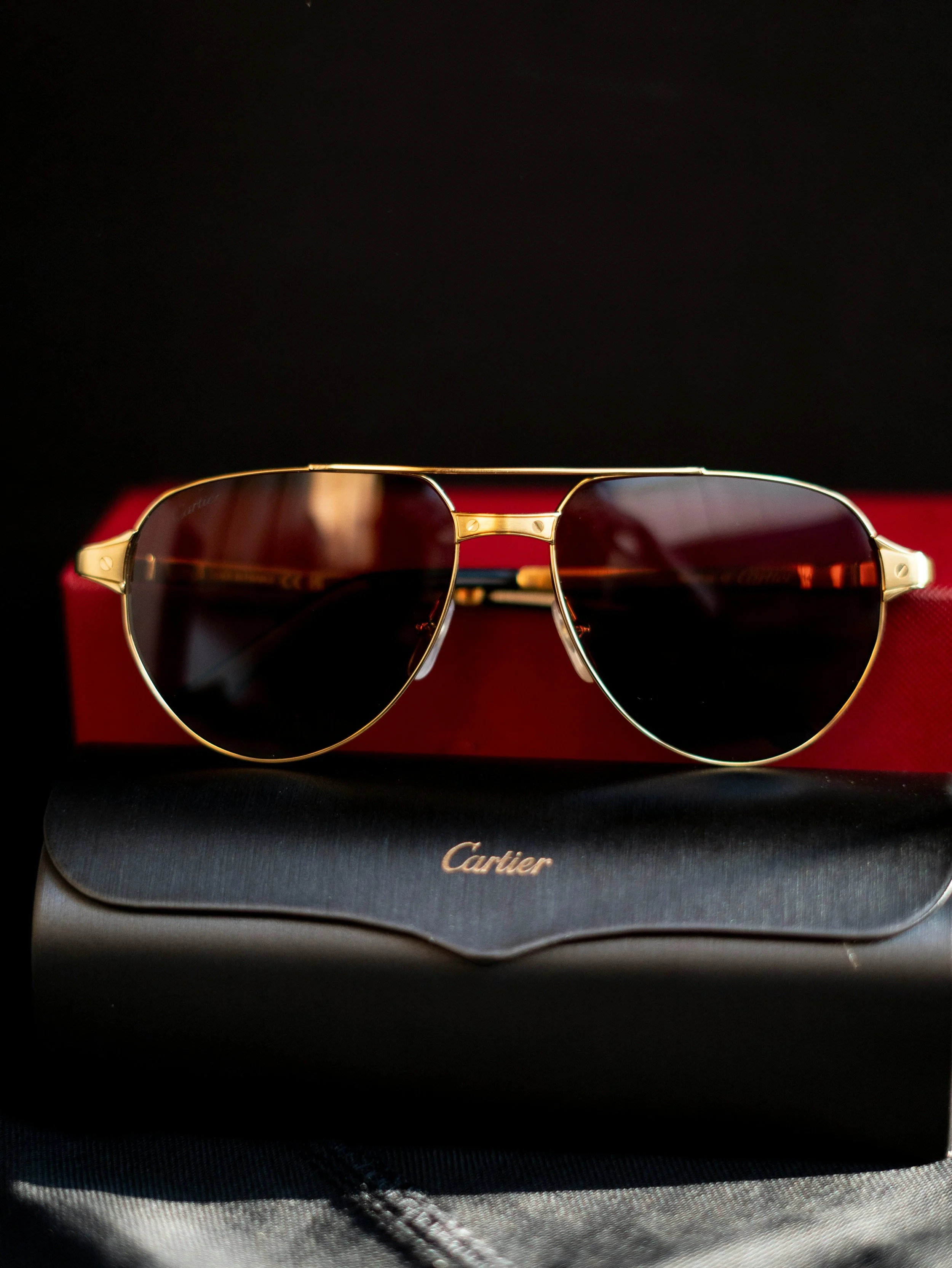 A pair of Cartier sunglasses with dark lenses and gold frames on a black case.