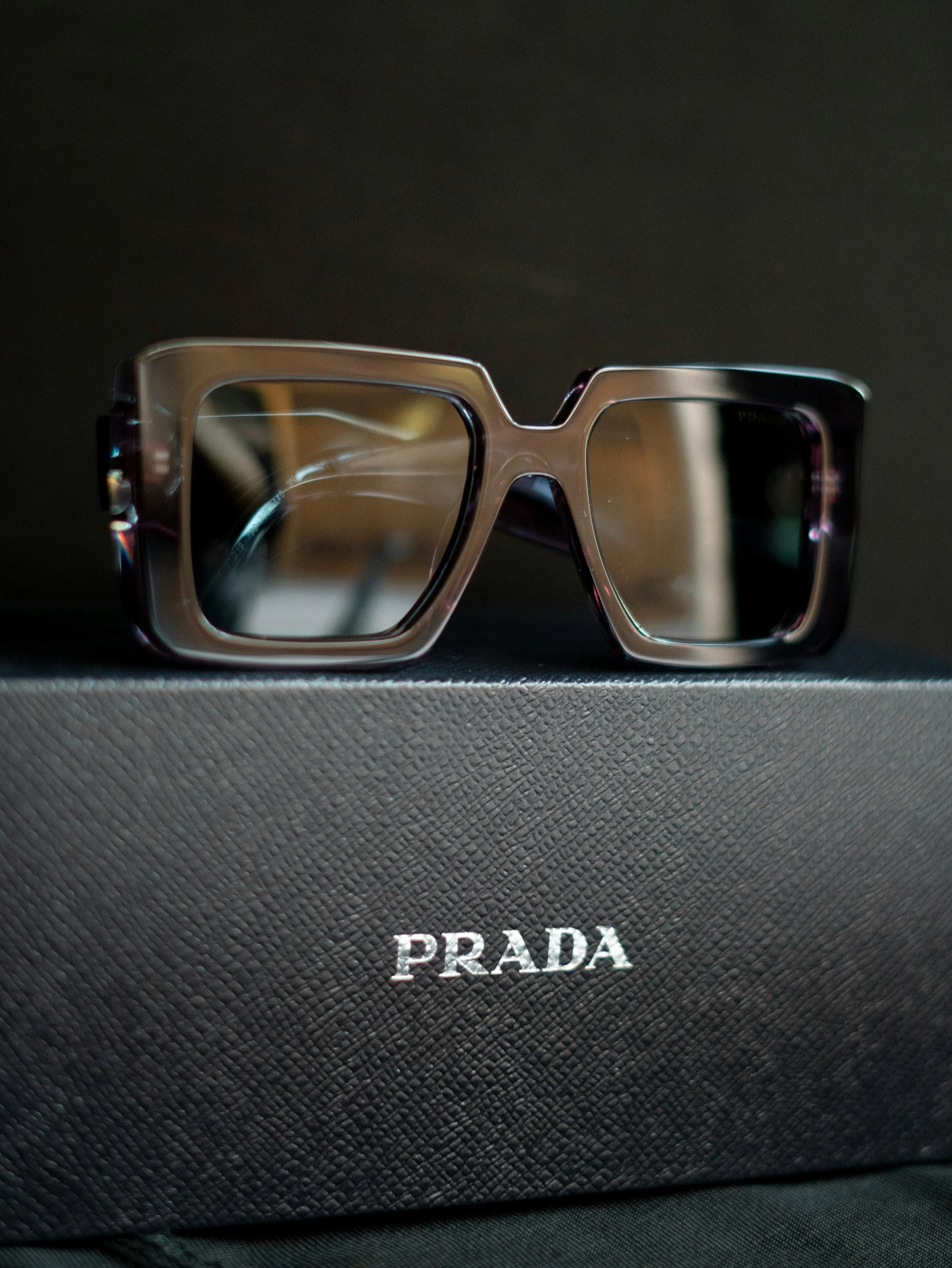 Black Prada sunglasses with tinted lenses, resting on a textured black Prada box with silver text.