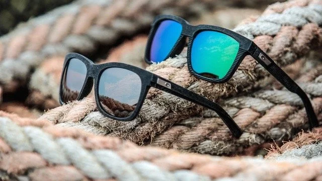 Pair of black sunglasses and a pair of black sunglasses with blue mirrored lenses resting on thick, weathered ropes