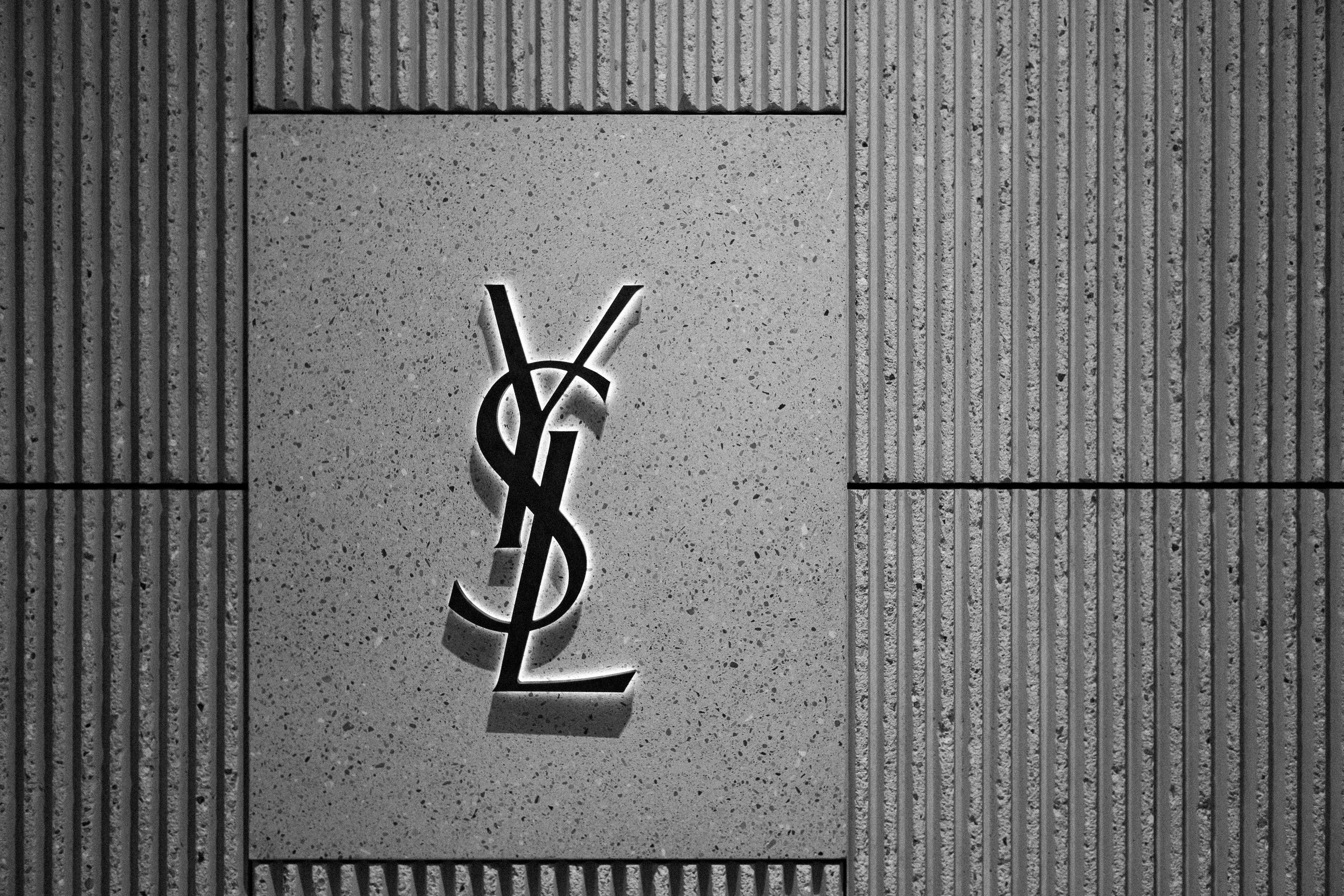 Yves Saint Laurent logo cutout with backlighting on a textured concrete wall.