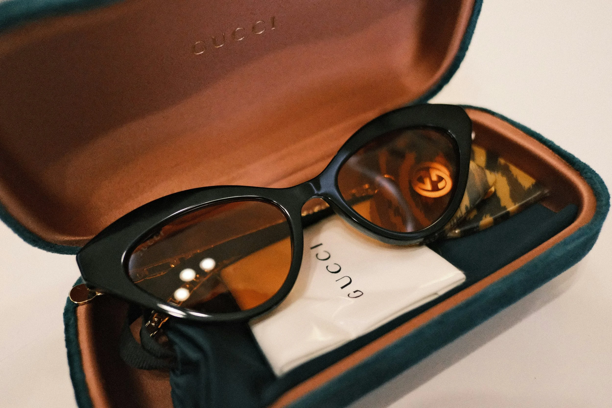 A pair of black Gucci sunglasses with orange-tinted lenses inside a blue and brown Gucci case, with a white Gucci cloth inside.