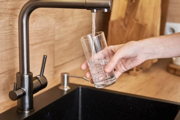 Person filling a glass with water from a kitchen faucet.
