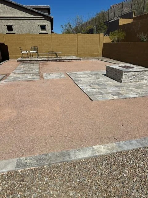 Backyard with a mix of gravel, concrete, and brick paving, two wooden chairs, a raised concrete platform, and a wooden fence.
