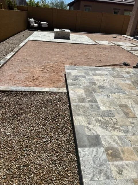 Backyard with different sections of ground coverings including gravel, brick pavers, and dirt, with a wooden fence and two parked cars in the background.