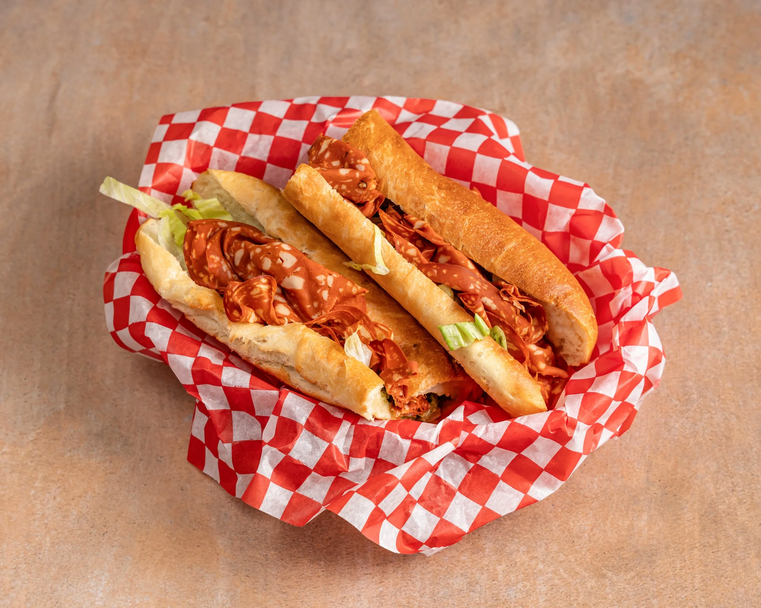 Three hot dogs in buns with mustard, served in a red and white checkered basket.