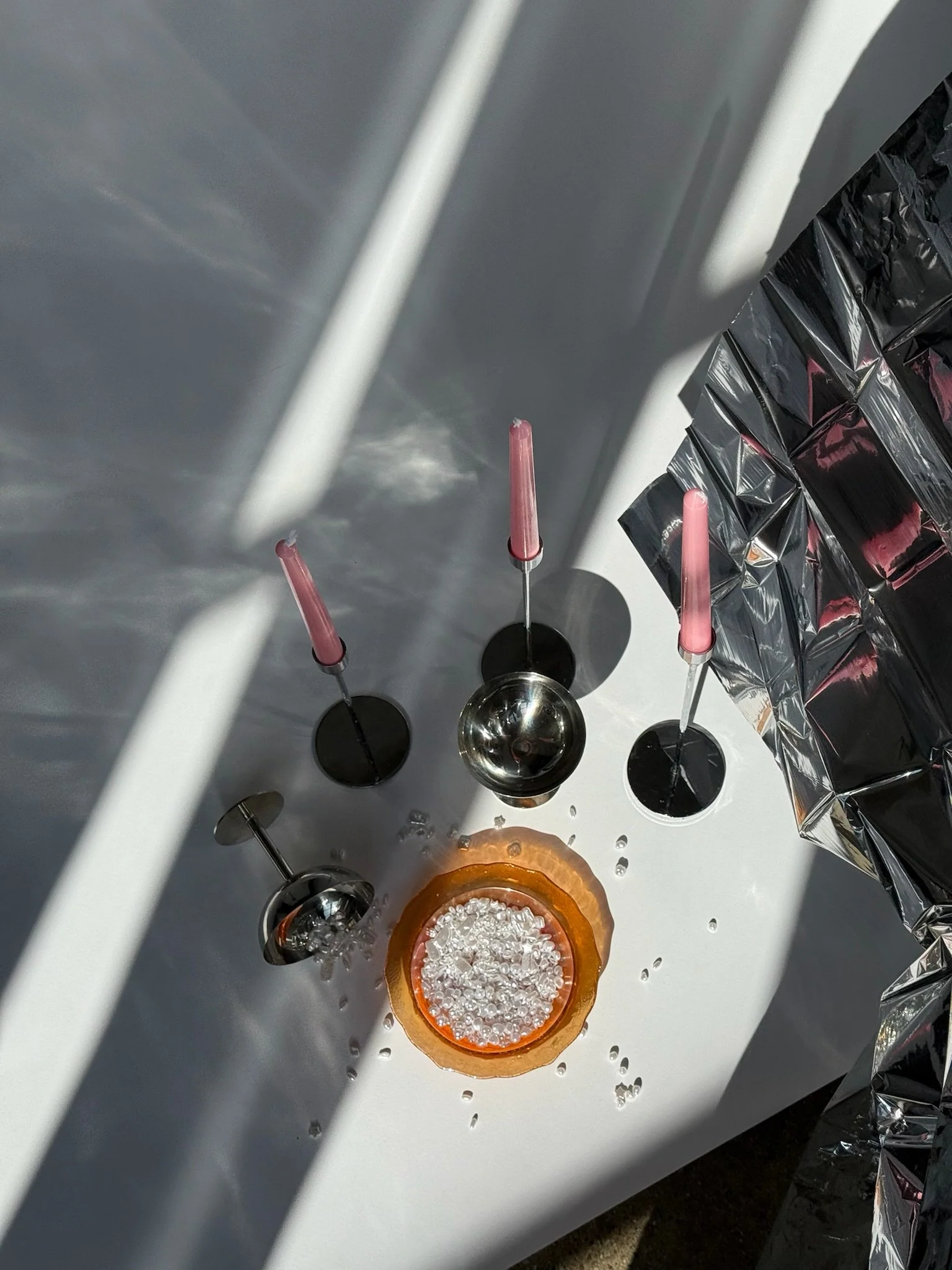 Lab setup with three small bottles containing pink liquid, a round metallic object, and a container filled with small clear beads, all on a white surface with metallic and black materials nearby.