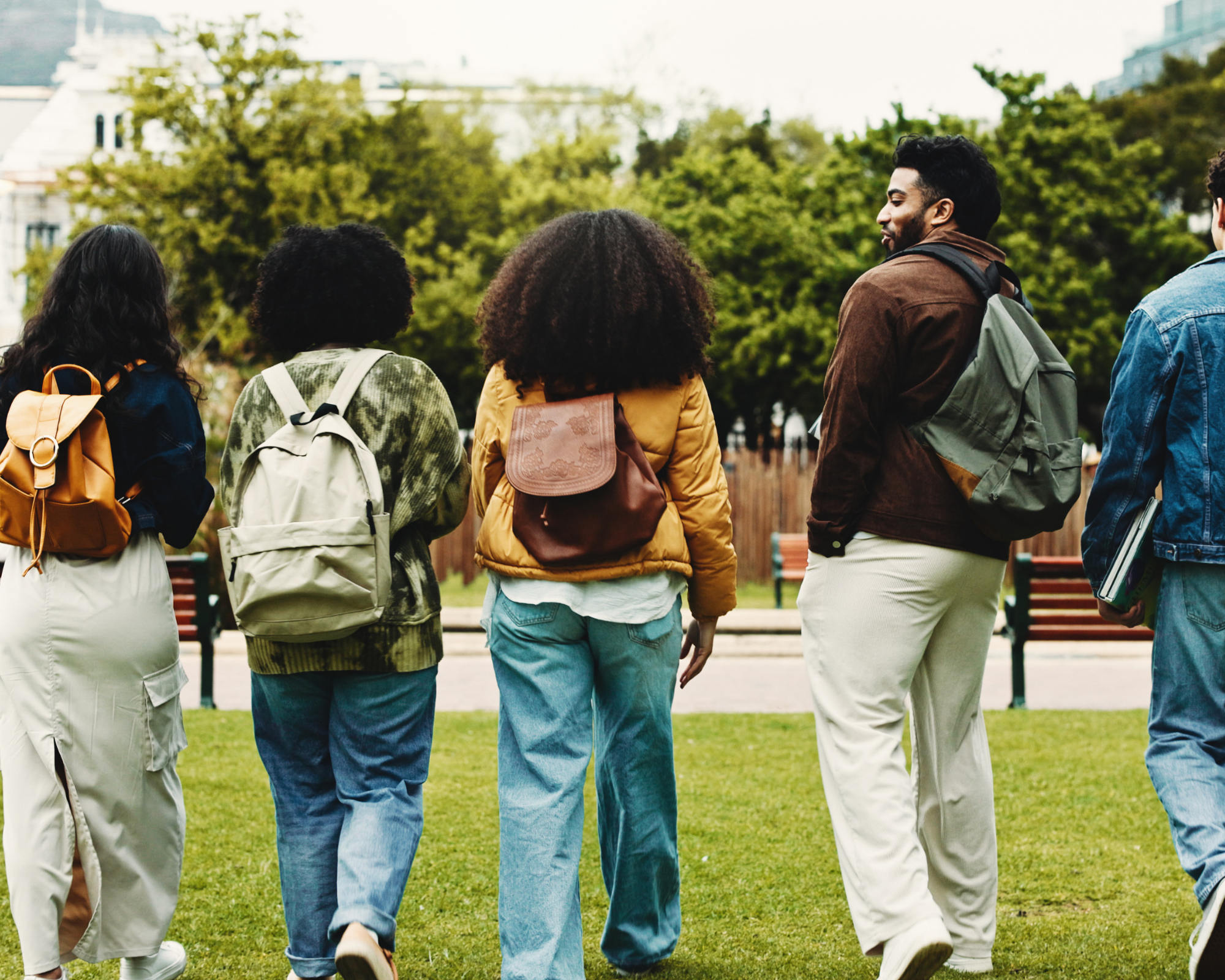 Group of diverse young adults walking together in a park with green trees and benches.