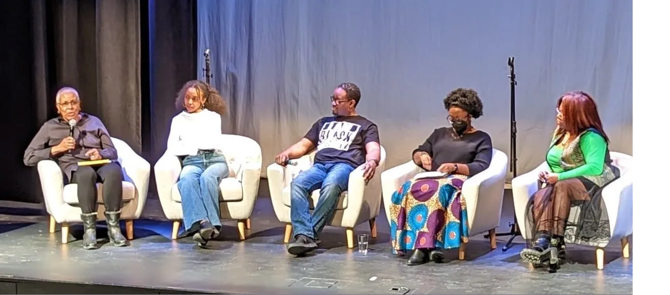 Panel of four women and one man sitting in white armchairs on stage during a discussion, with a plain backdrop behind them.
