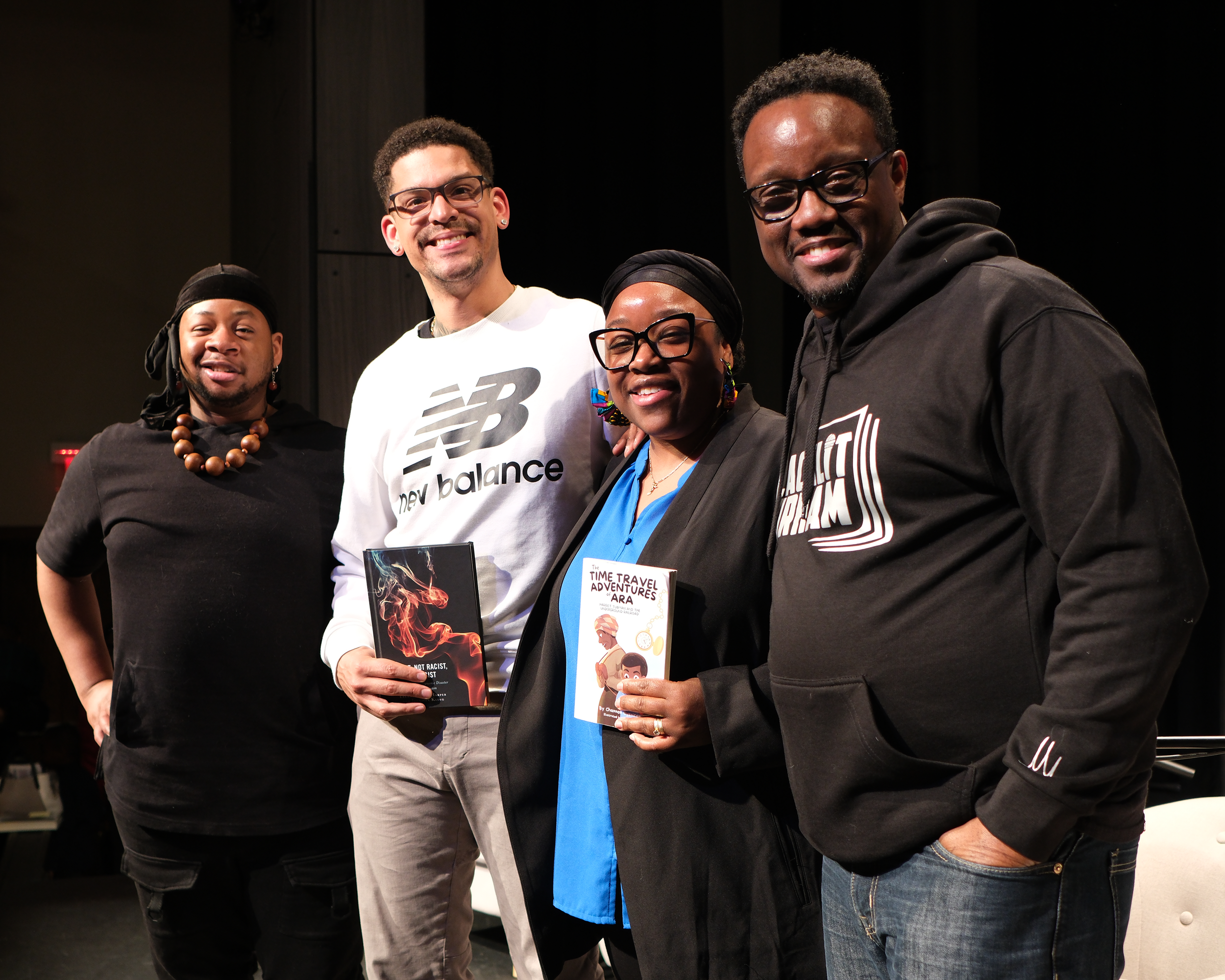 Four people standing together on stage, holding books, smiling at the camera.