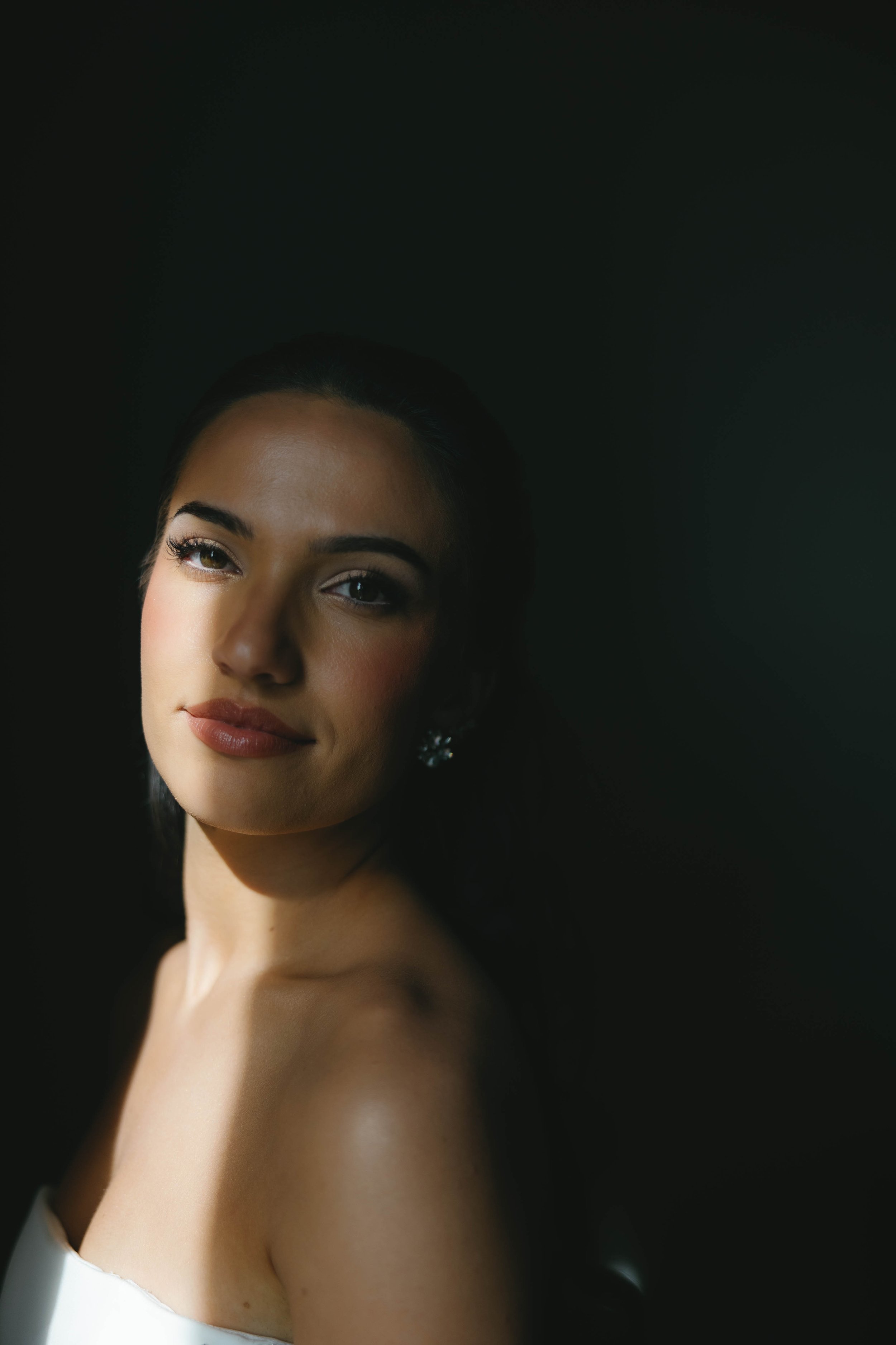 Portrait of a woman with dark hair, wearing earrings, against a dark background.