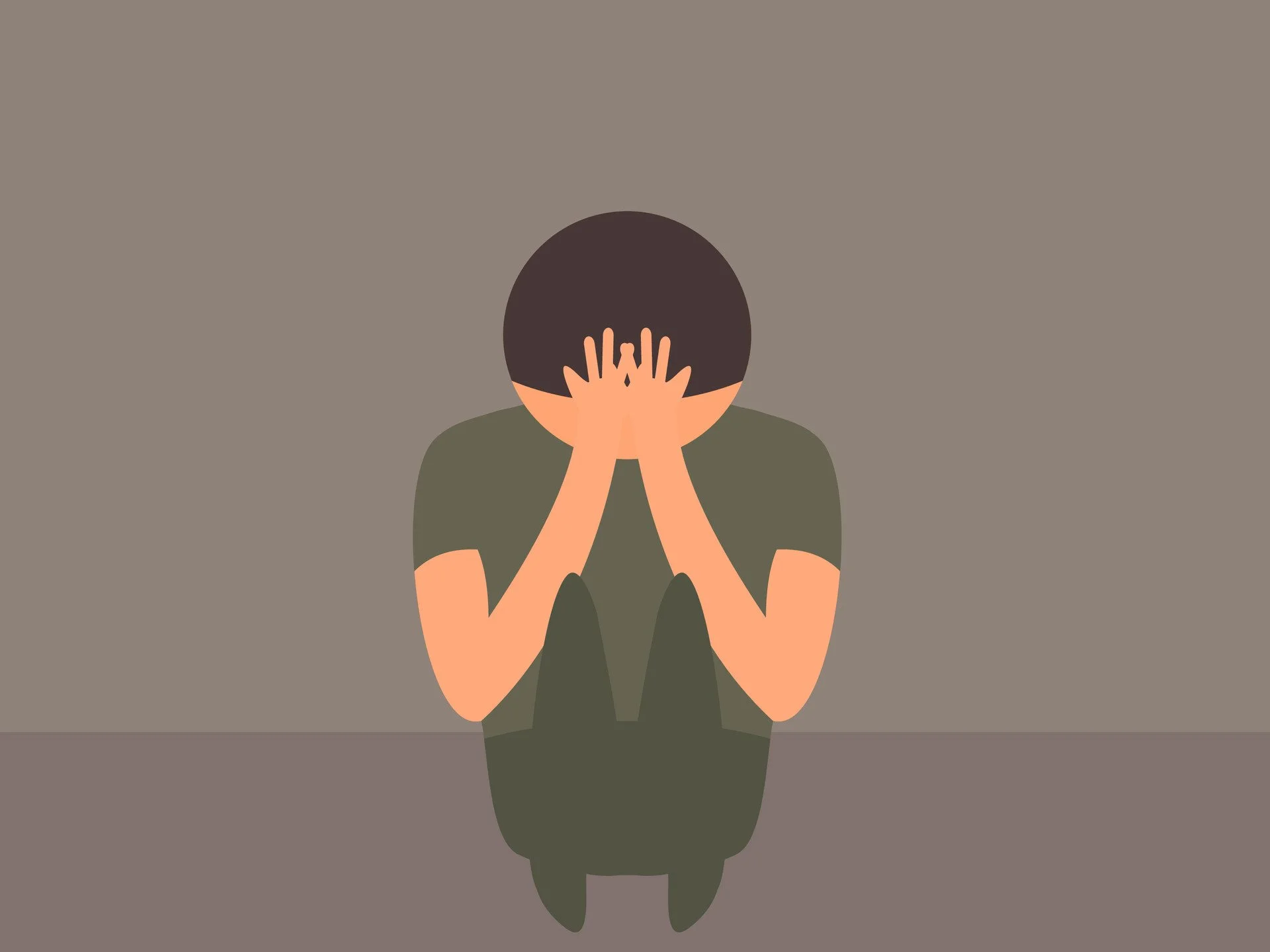 Person sitting on the floor with knees up, covering their face with their hands, in a plain room.