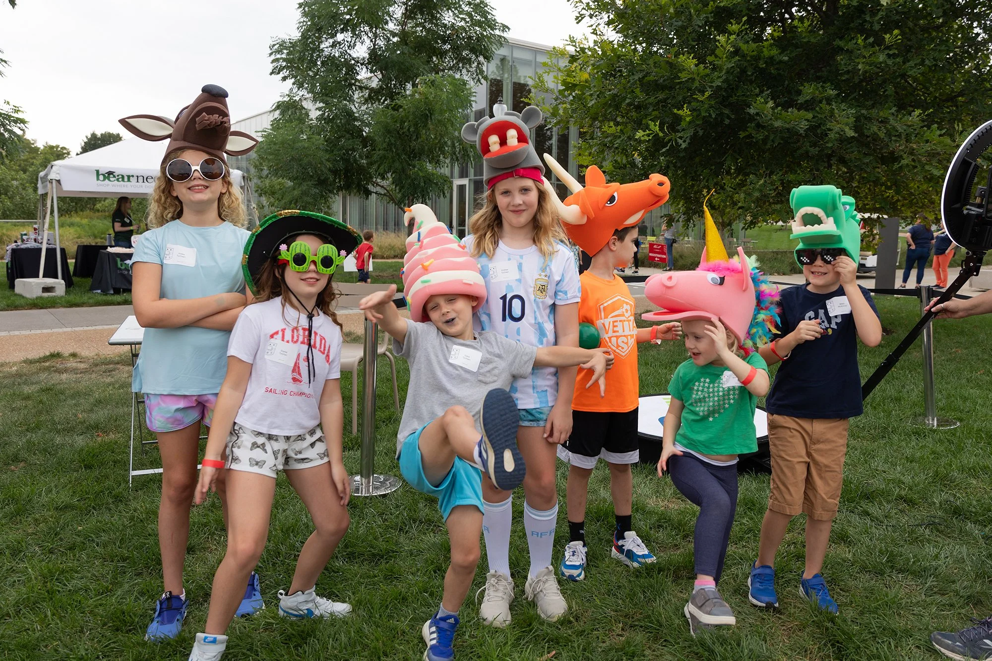 Group of children wearing colorful costumes and animal-themed hats at an outdoor event
