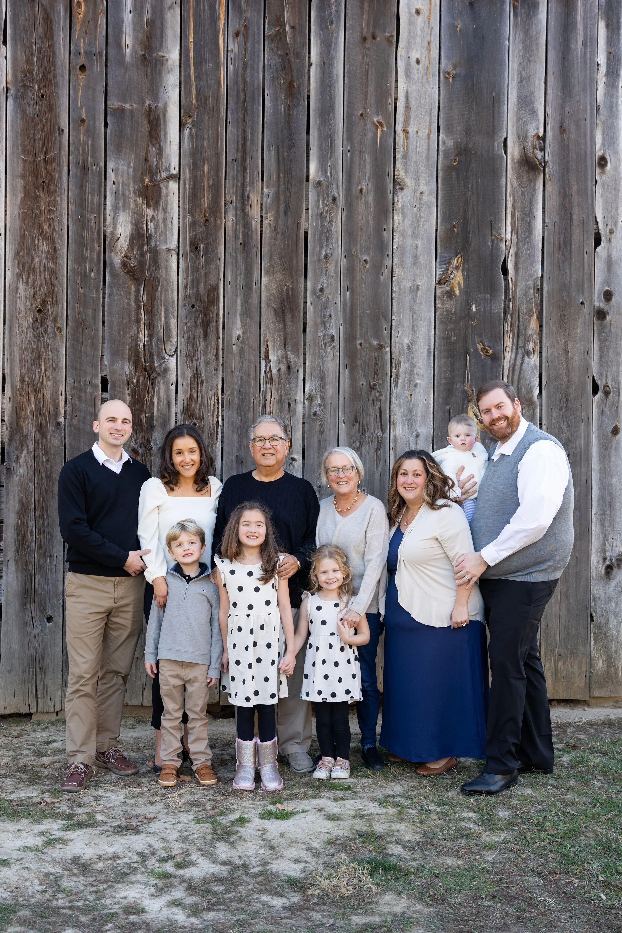Family photo of ten people, including children and grandparents, standing in front of a large wooden barn wall, smiling at the camera.