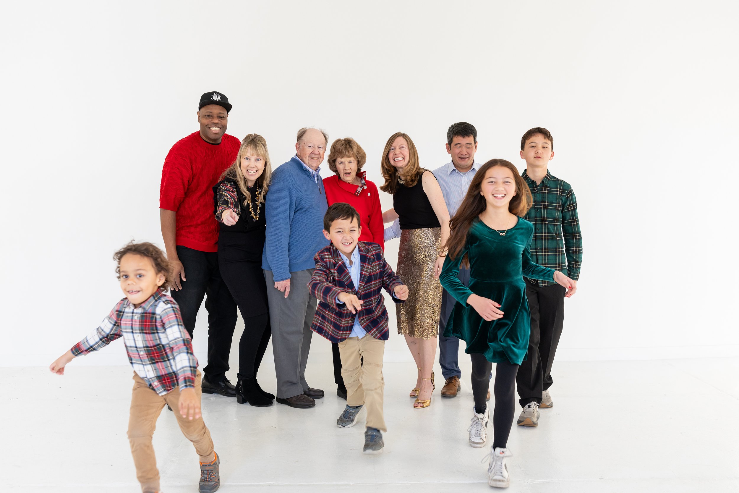 A diverse group of people, including children and adults, smiling and running towards the camera in a white room