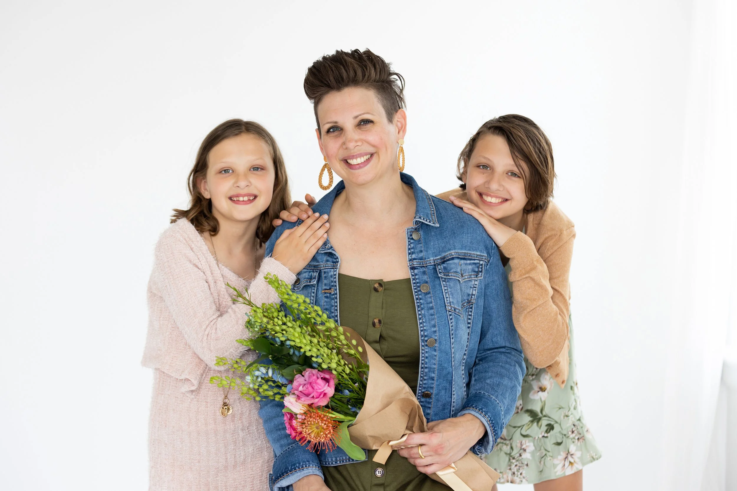 A woman holding a bouquet of flowers, flanked by two children, all smiling and posing together against a white background.