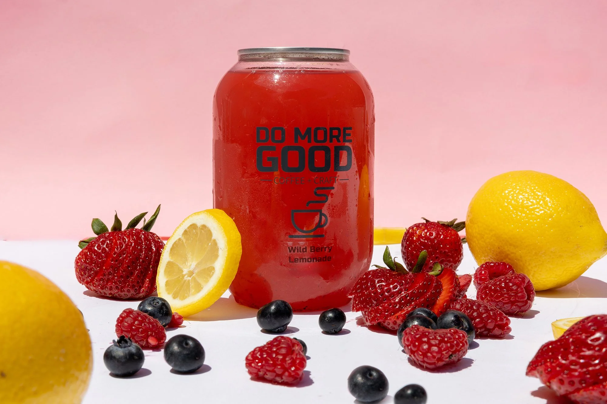 A can of Wild Berry Lemonade surrounded by strawberries, blueberries, raspberries, and lemons on a white and pink background.