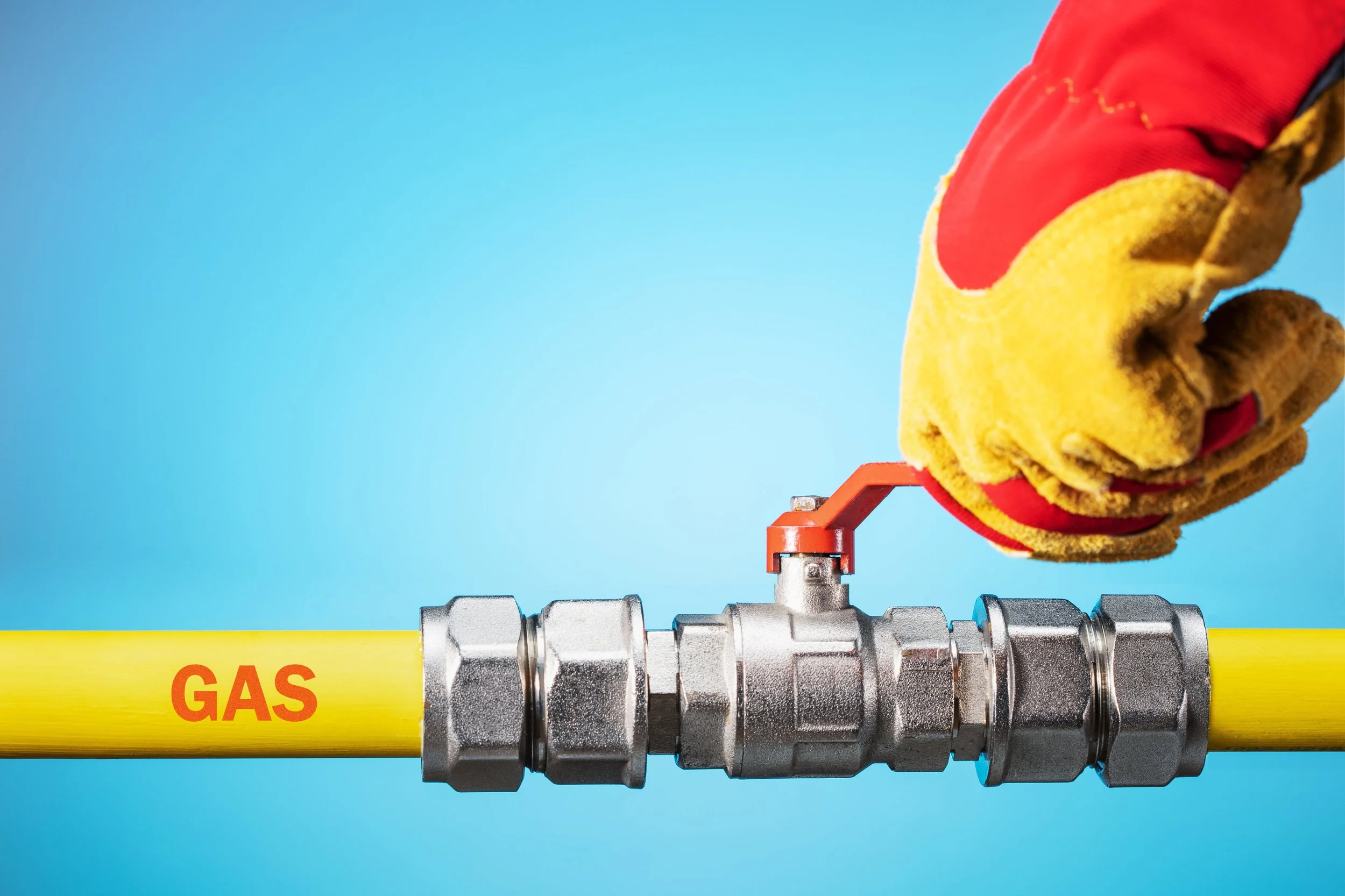 A person wearing yellow and red gloves opens a gas valve attached to a yellow gas pipe labeled 'GAS' against a blue background.