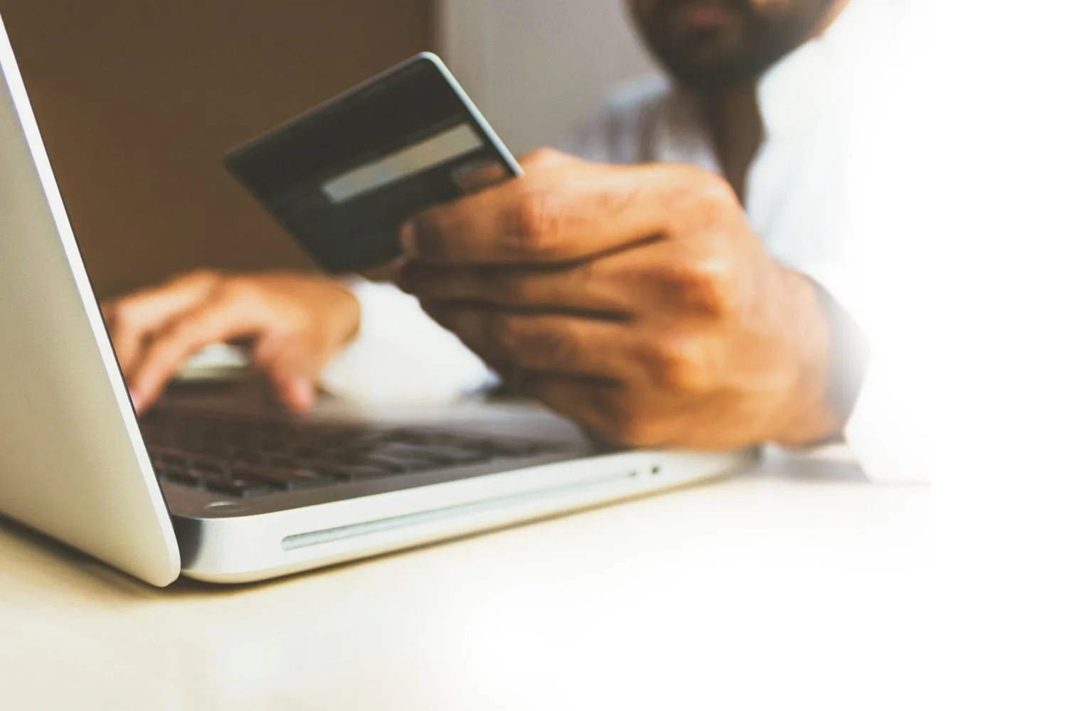 Person holding a credit card and typing on a laptop keyboard