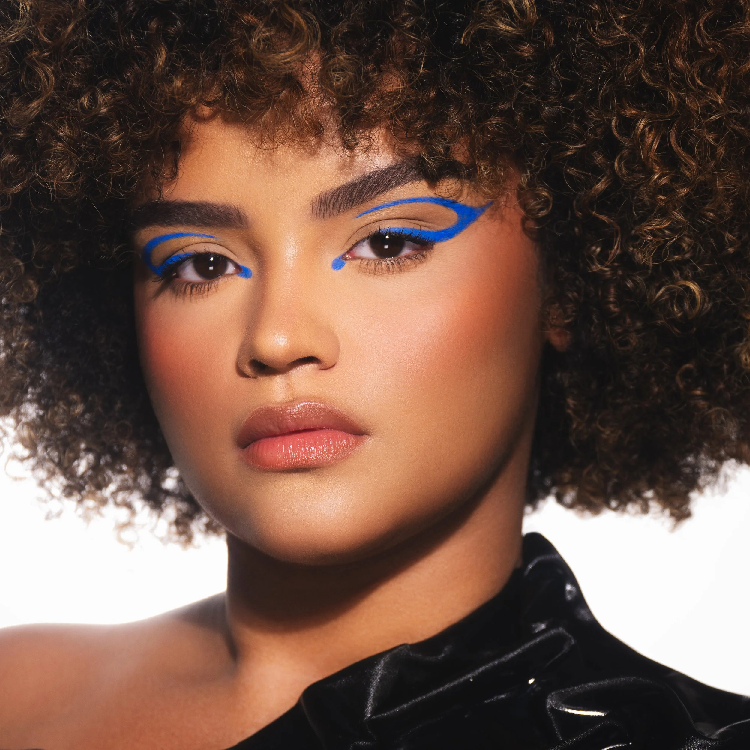 A woman with curly hair, bold makeup, and blue artistic eyeliner.