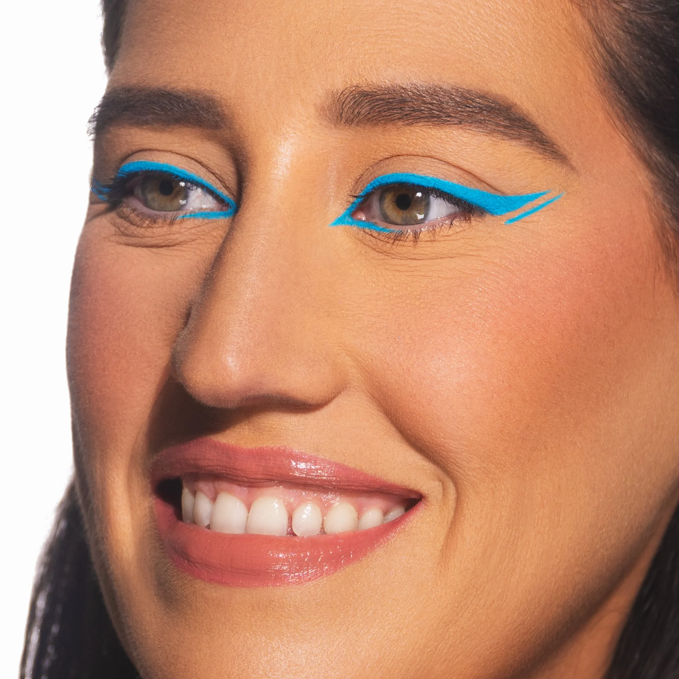 Close-up of a woman smiling with bright makeup, featuring vivid blue eyeliner in an artistic, winged style.