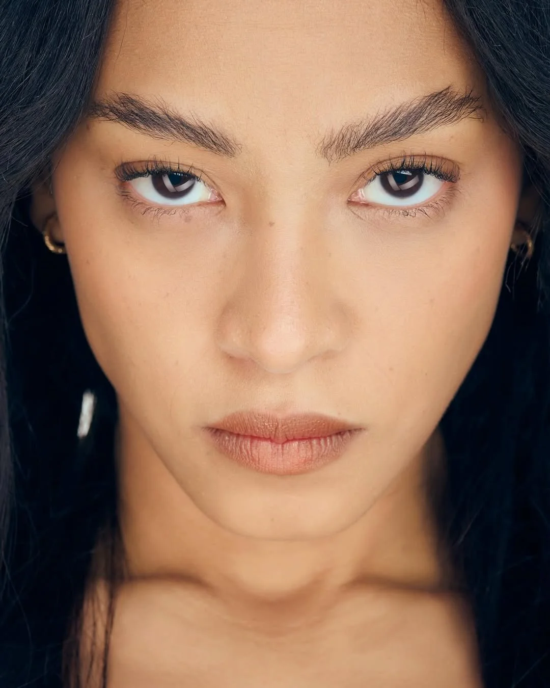Close-up of a woman's face with dark hair, almond-shaped eyes, light makeup, and full lips.