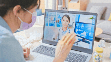 Person in medical mask participating in a virtual doctor's consultation through a laptop