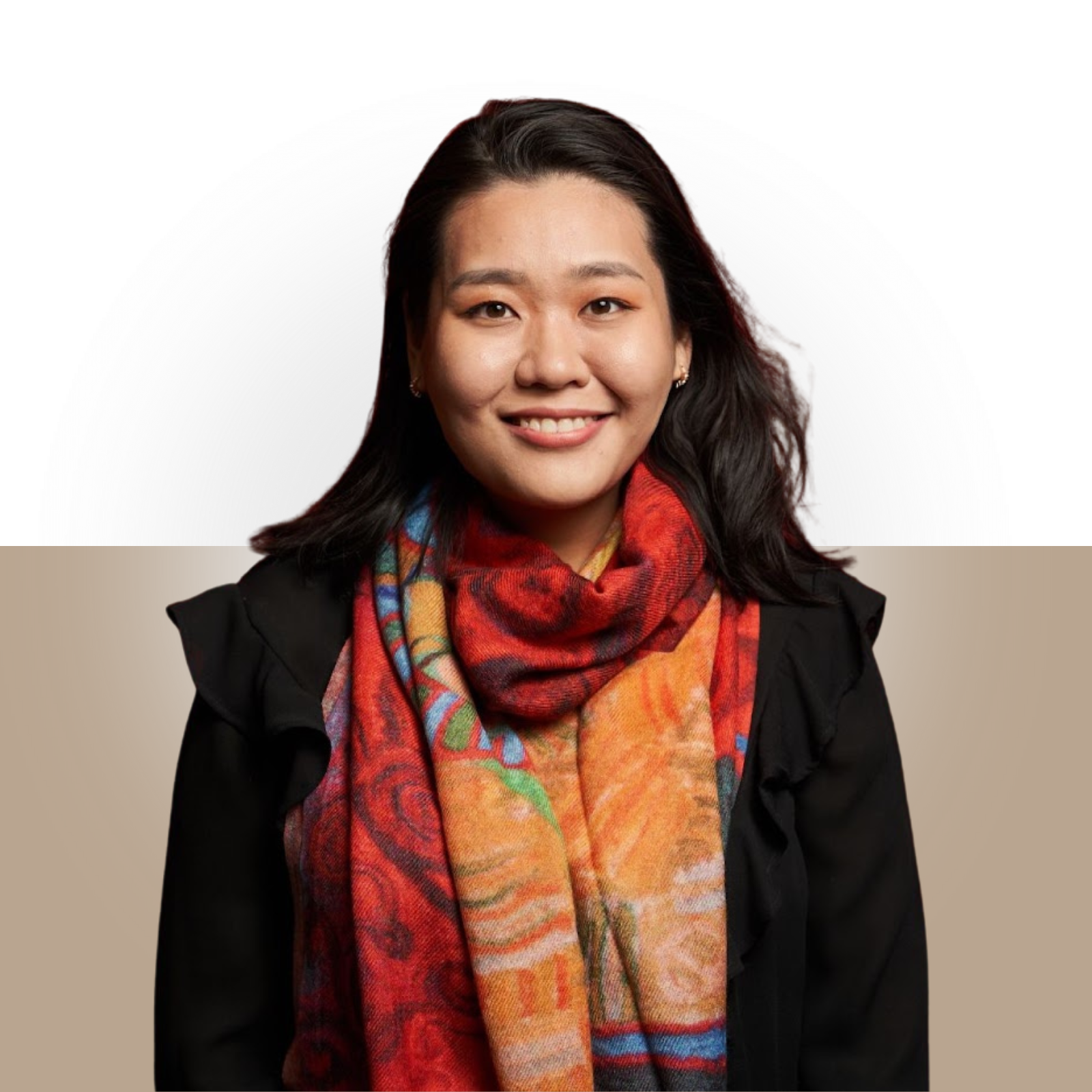 Portrait of a smiling woman with dark hair, wearing a black jacket and colorful scarf against a light and dark background.