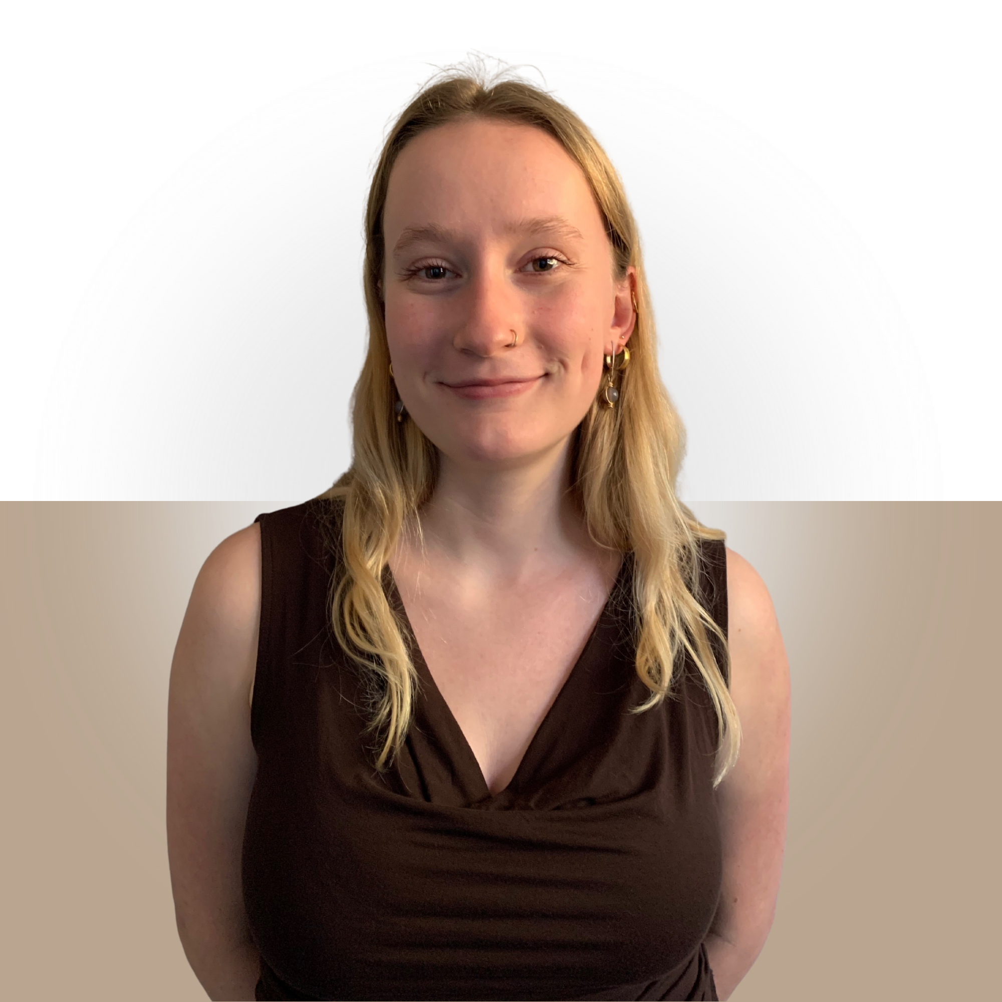 A woman with light skin, long wavy blonde hair, and a nose piercing, smiling, wearing gold earrings and a sleeveless dark brown top, standing in front of a gradient background blending white and beige.