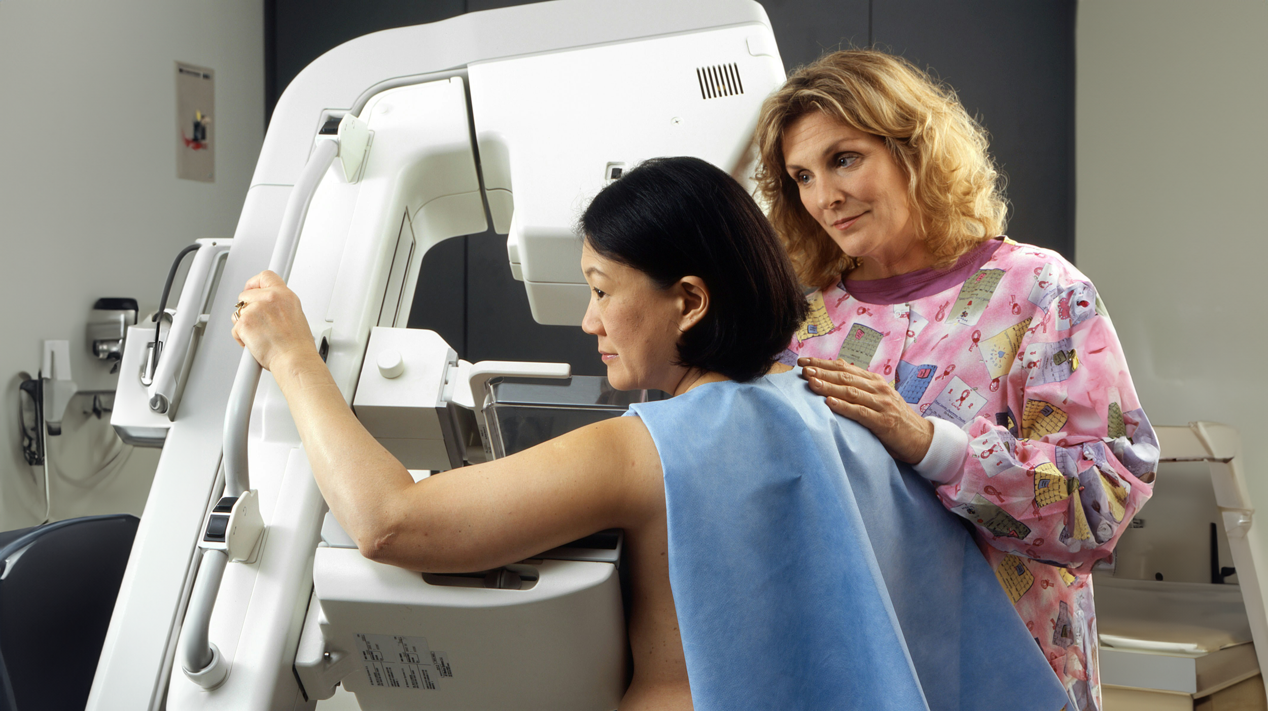 A woman undergoing a medical imaging procedure, assisted by a healthcare professional.