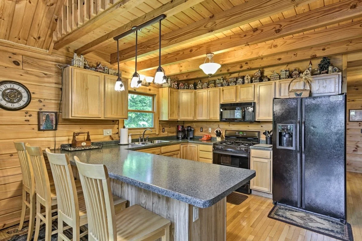 Kitchen with wooden cabinets, black refrigerator, stove, microwave, and a kitchen island with four chairs.