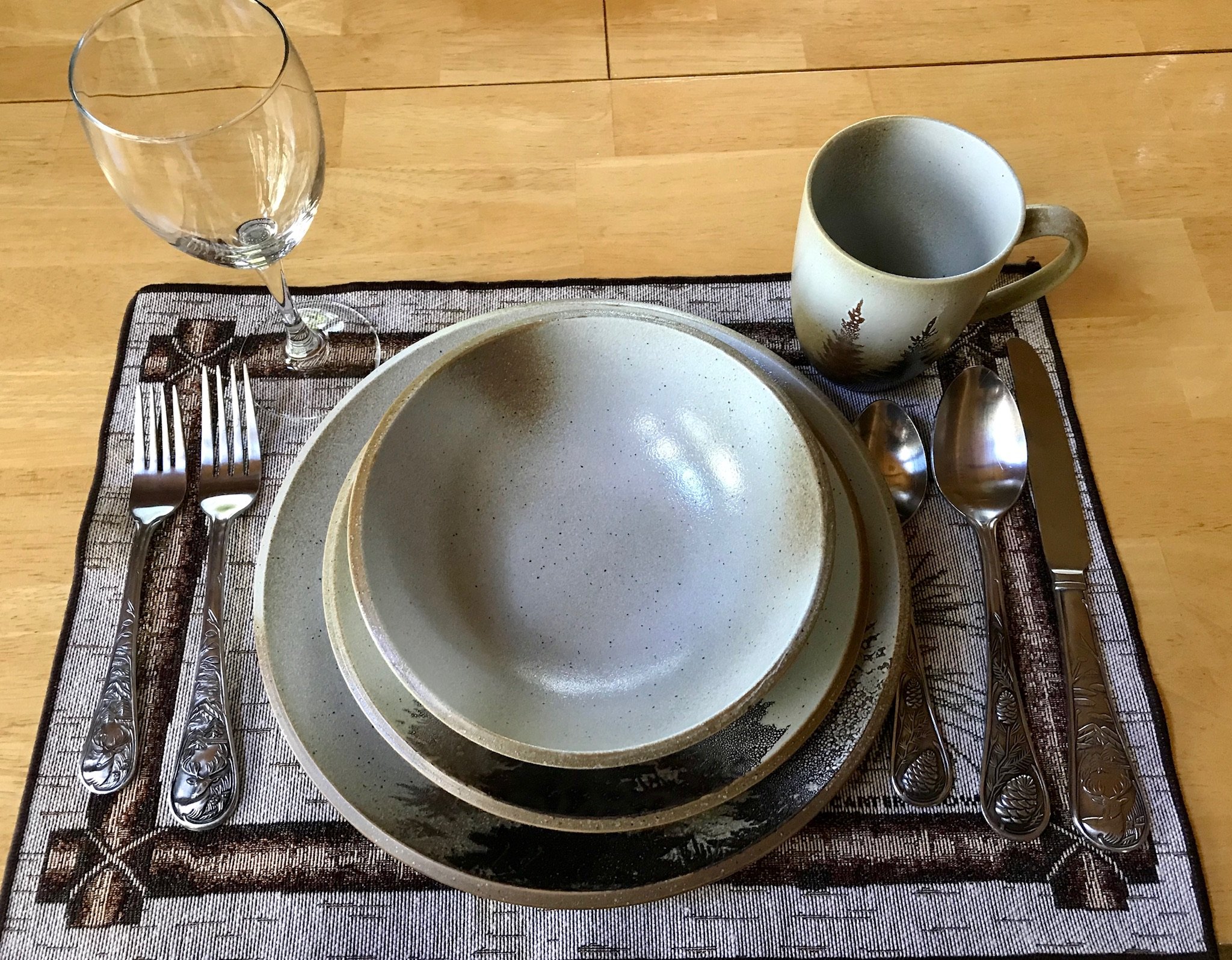 Empty plates, a glass, a mug, and silverware arranged on a table with a decorative placemat.