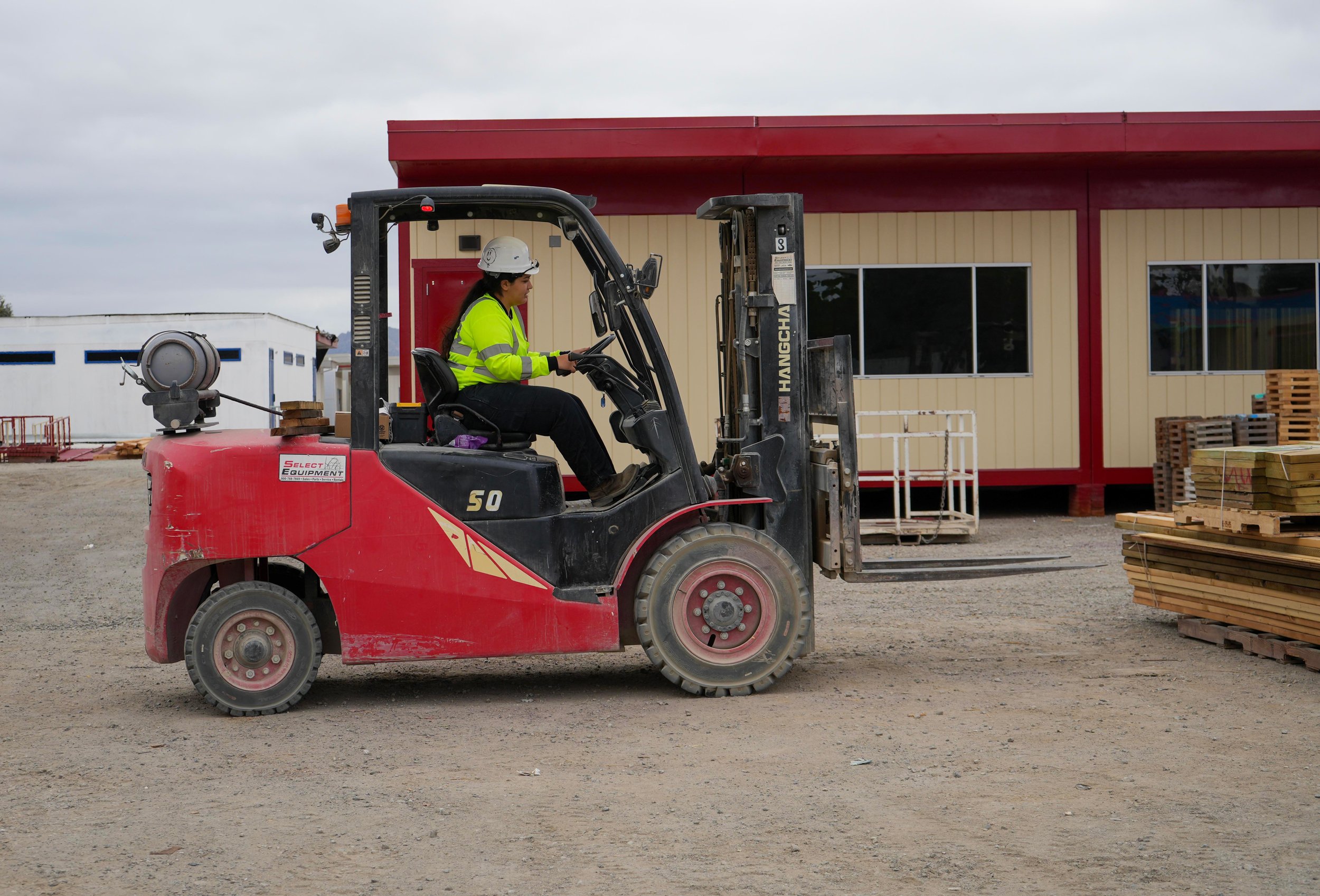 Construction worker operating a forklift at a construction site with a beige building in the background.