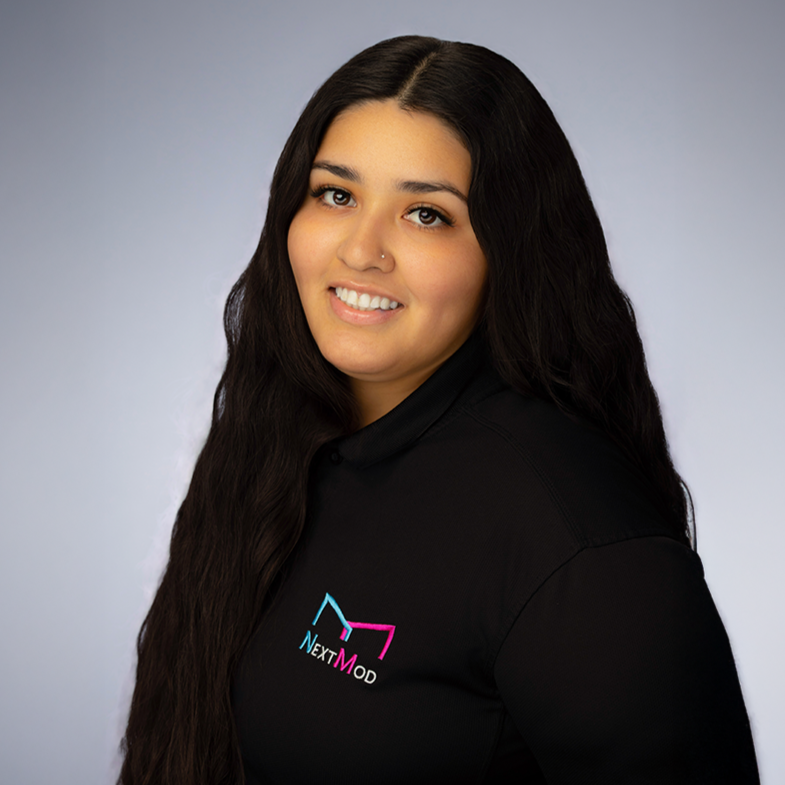 Young woman smiling, wearing a black polo shirt with a colorful 'NextMod' logo, standing against a plain gray background.