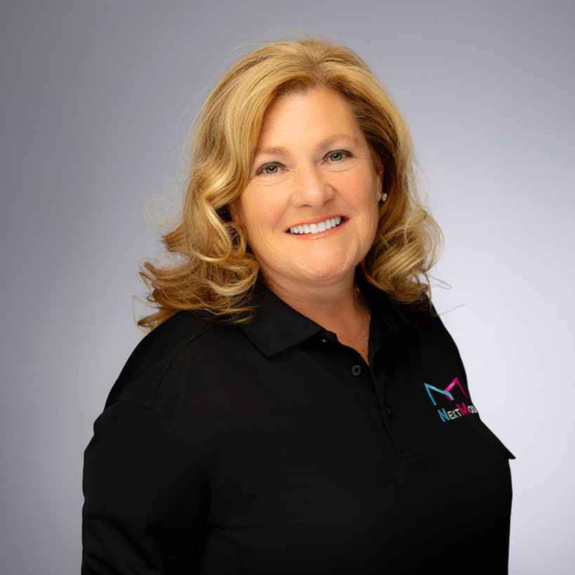 Laura Zamora with blonde hair wearing a black polo shirt with a "NextMod" logo on it, smiling at the camera against a light gray background.