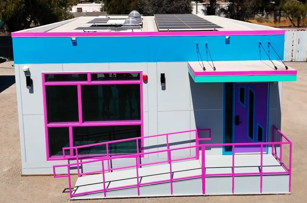 Colorful modern building with blue, pink, and teal accents, large glass windows, a door, and solar panels on the roof.