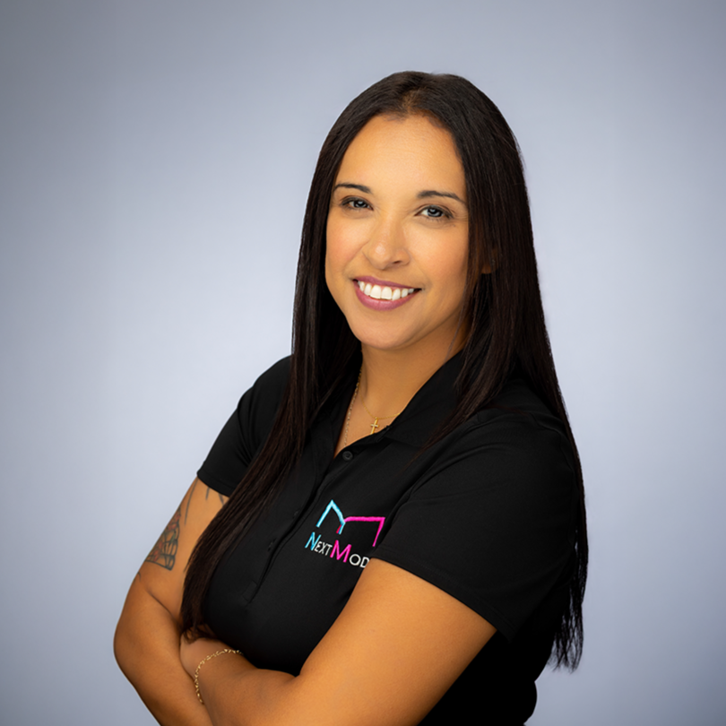 A woman with long dark hair wearing a black polo shirt with the 'NextMod' logo in cyan, pink, and white, against a gray background.
