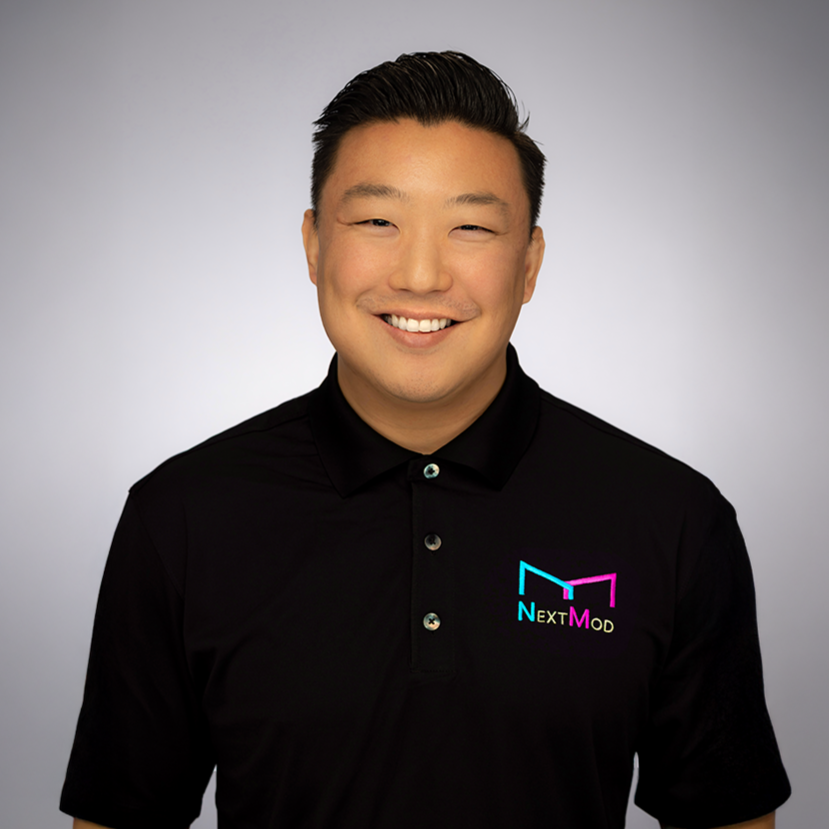 A smiling man wearing a black polo shirt with a "Next Mod" logo, standing against a neutral background.