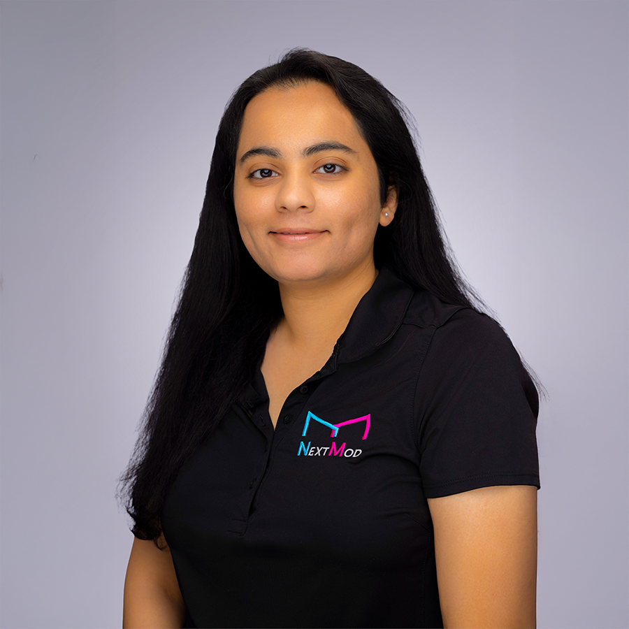A woman with long black hair wearing a black shirt with a colorful logo that says "NextMod" standing against a plain gray background.