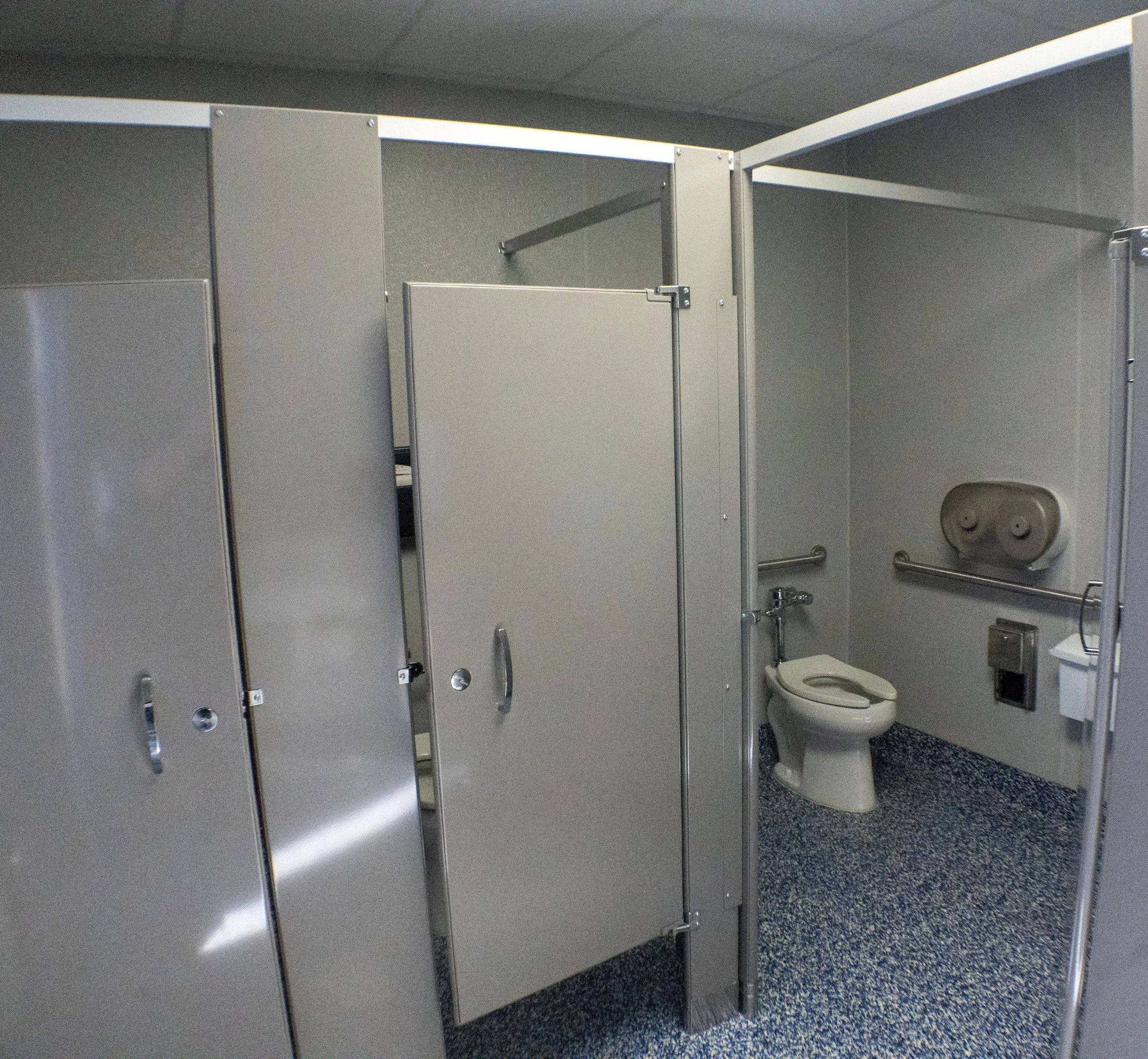 Public restroom with stalls, a toilet, paper towel dispenser, handrails, and soap dispenser.