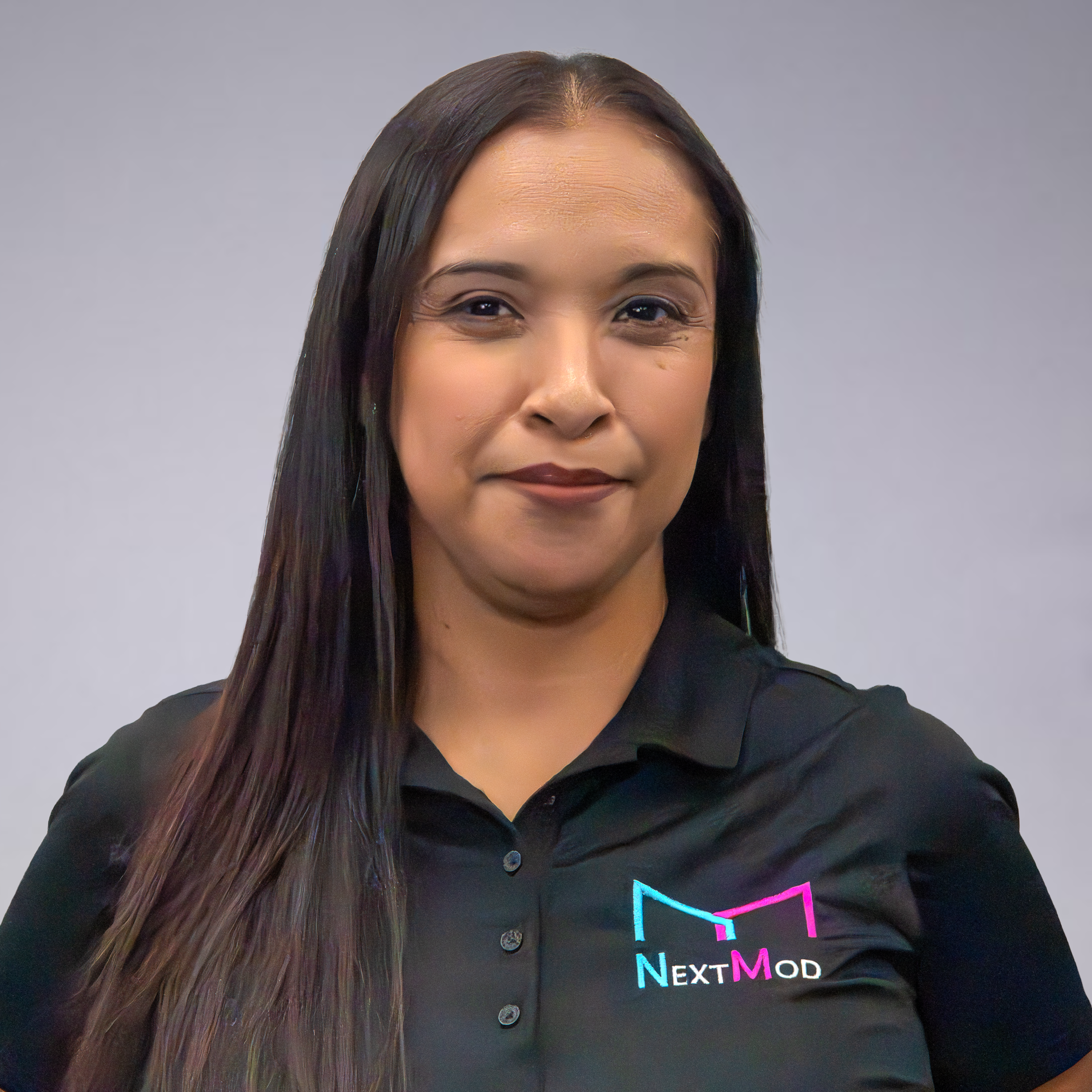 A woman with long dark hair wearing a black polo shirt with the 'NextMod' logo in cyan, pink, and white, against a gray background.
